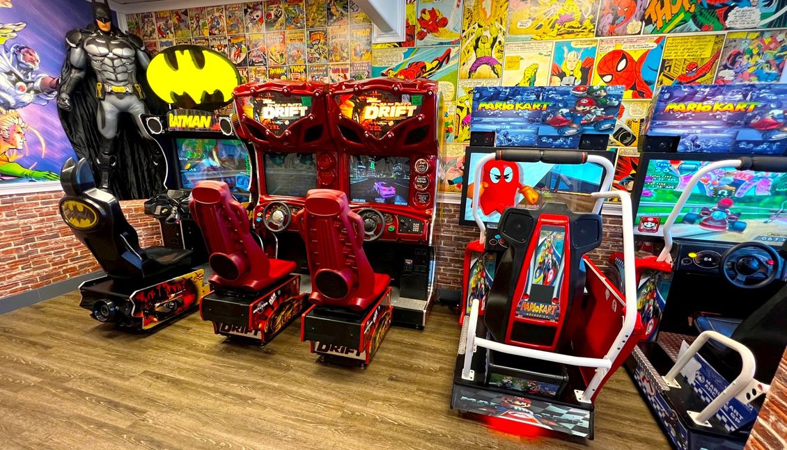 Arcade with Batman game, colorful racing machines, and red kiddie ride on a wooden floor