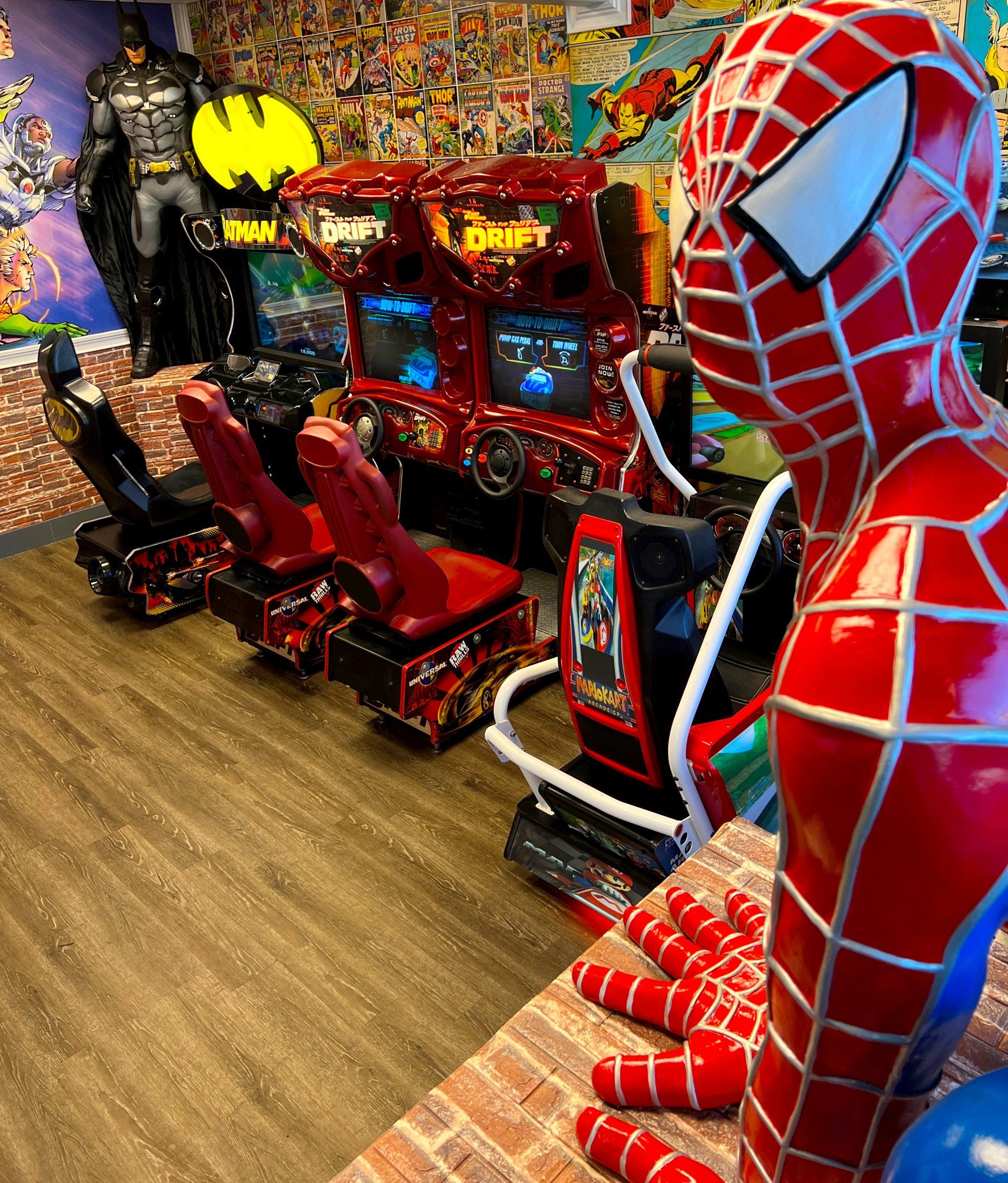 Spider-Man-themed arcade ride beside Batman figures in a game room