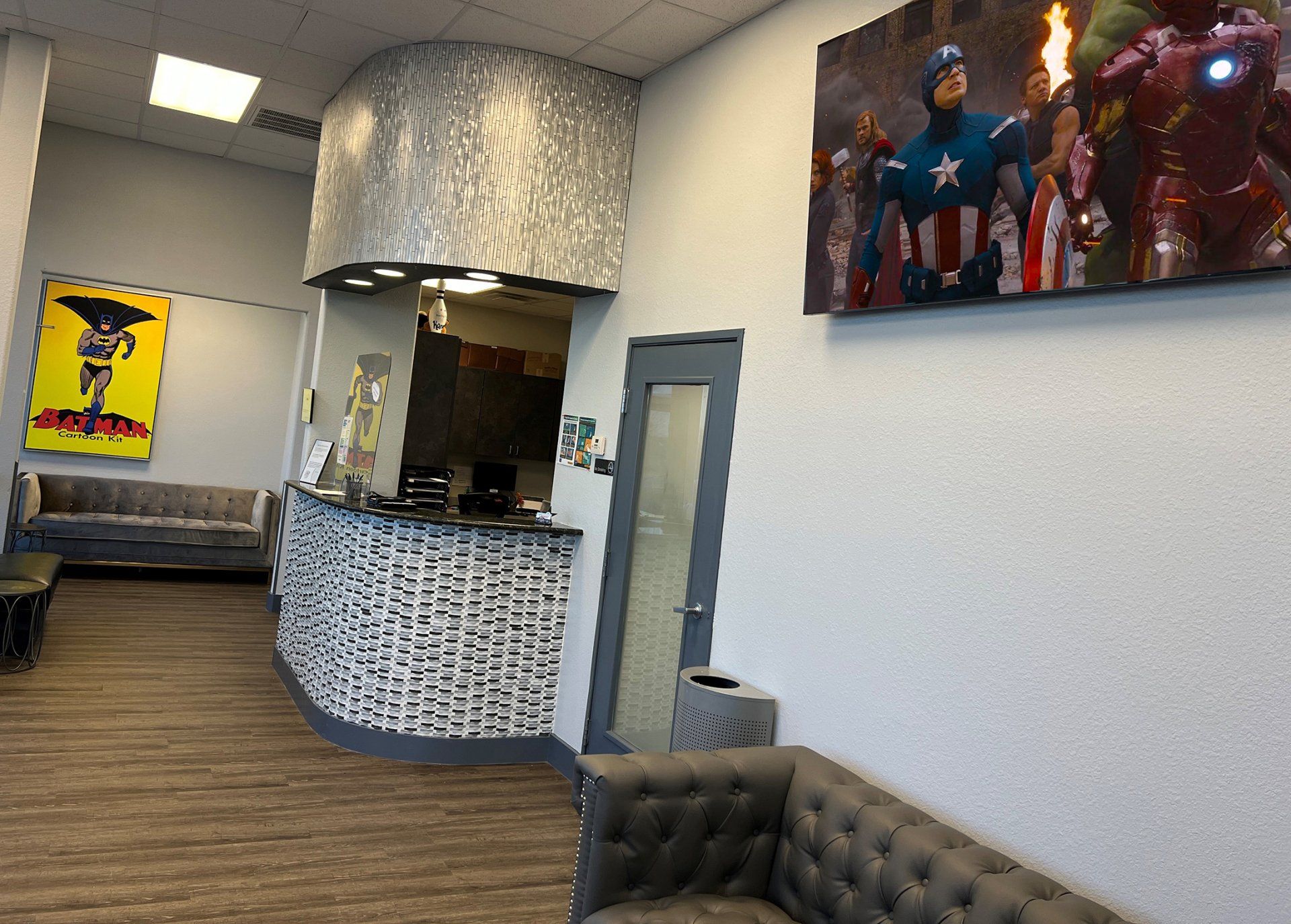 Modern lounge with curved bar, wood floor, wall art, and superhero poster on a white wall.