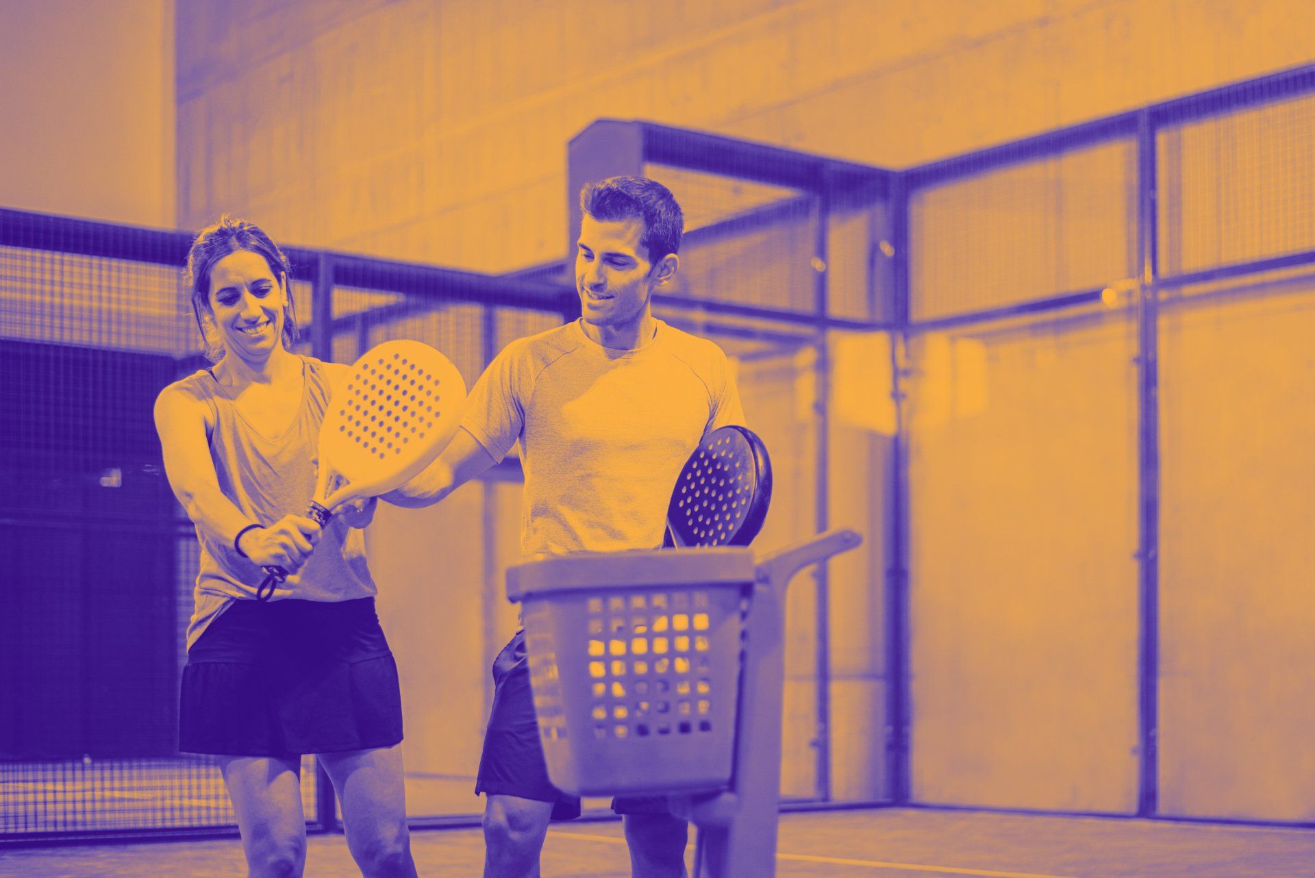 Een man en een vrouw houden tennisrackets en een wasmand vast op een tennisbaan.