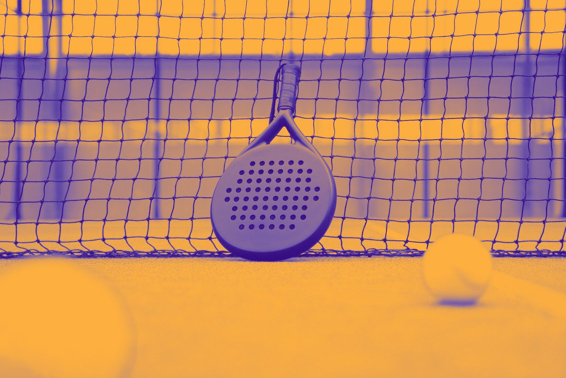 Een paddletennisracket ligt op een tennisbaan naast een tennisbal.