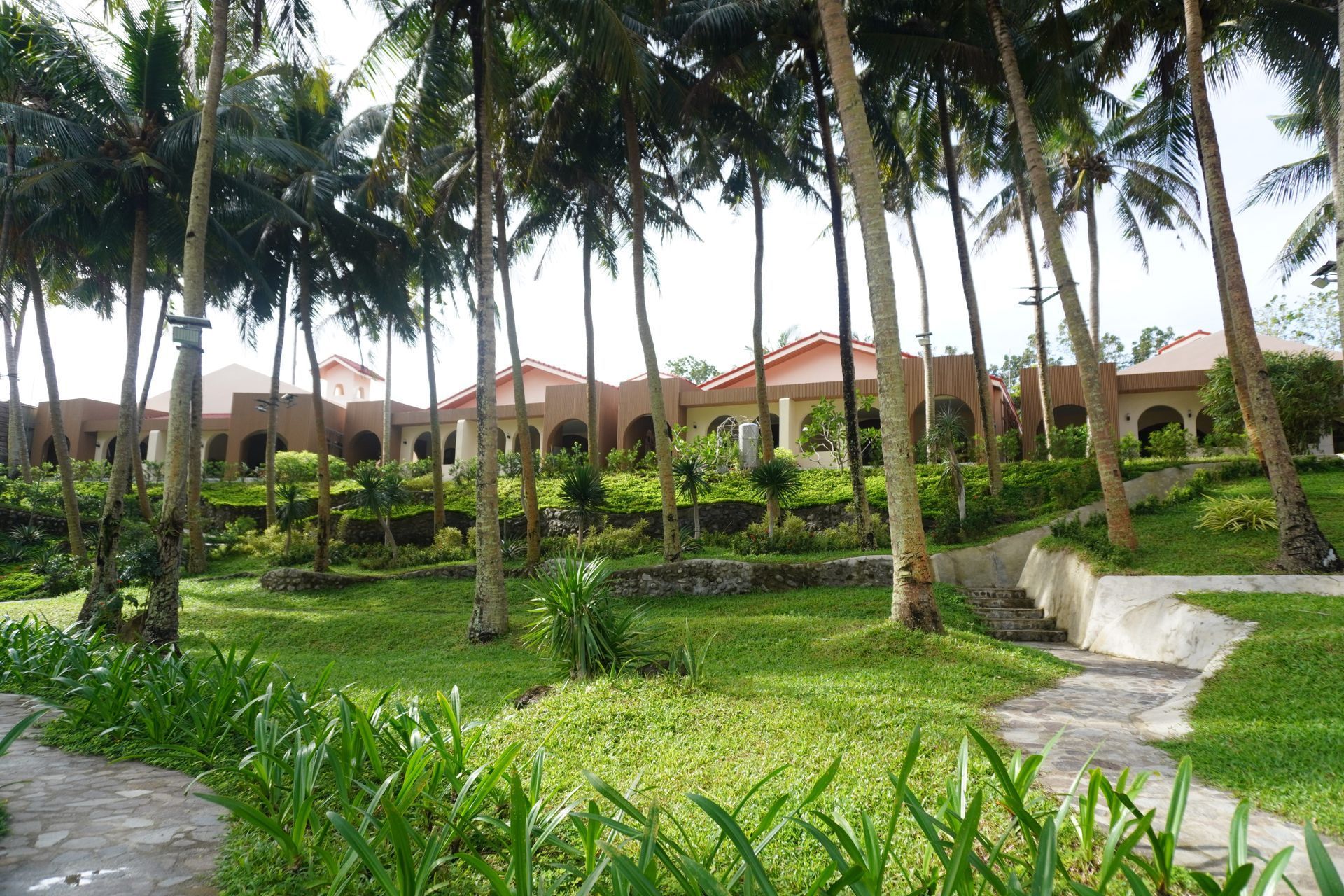 Tropical resort gardens with palm trees, green lawns, and villas in the background.