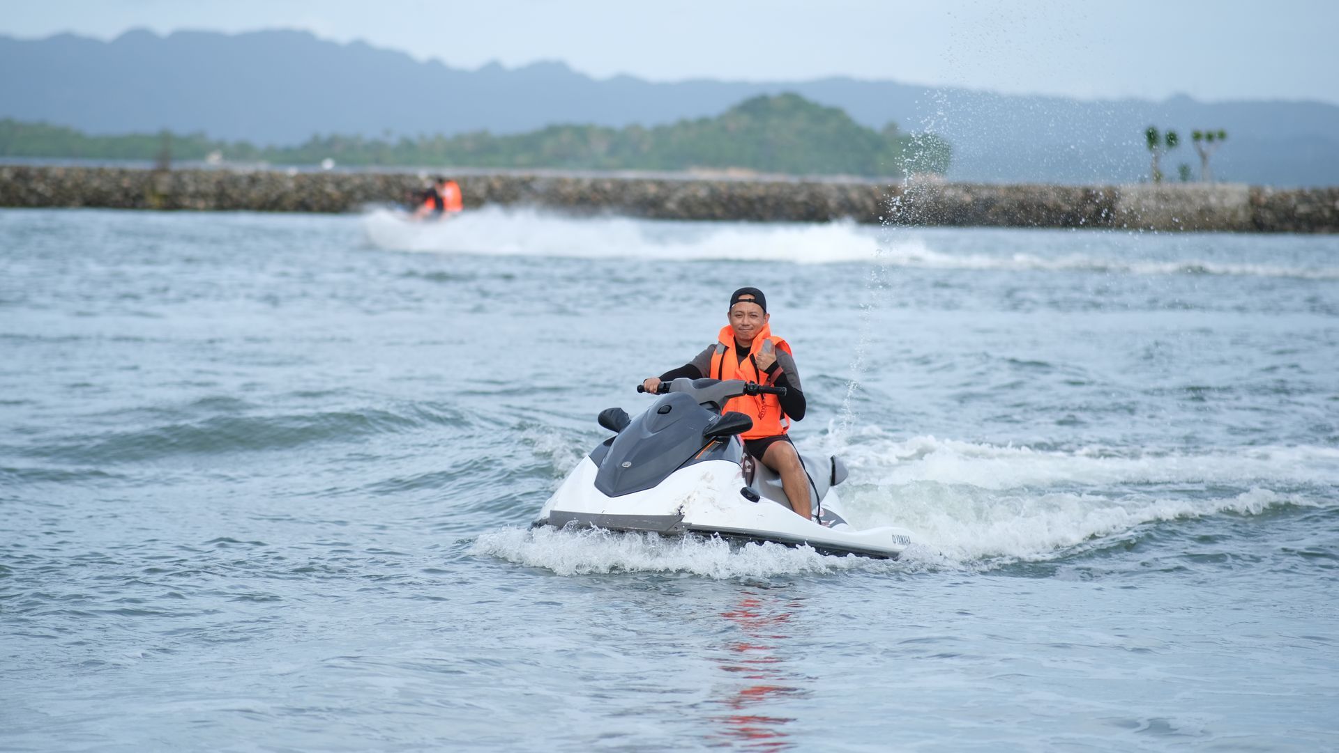 A person in dark athletic clothing paddles a long, light pink kayak across calm blue water.