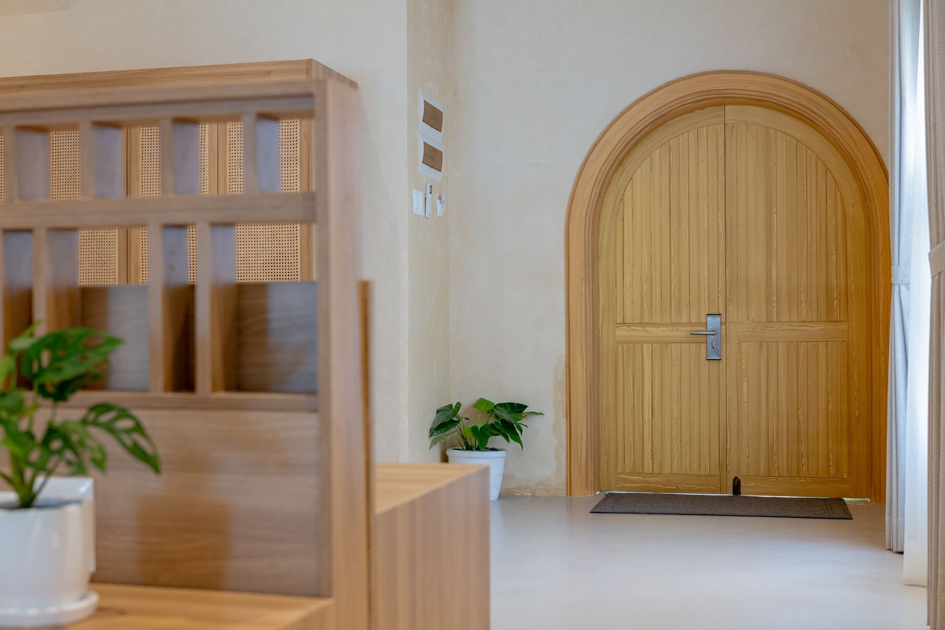 Arched wooden double door entryway with rattan shelf and monstera plant decor