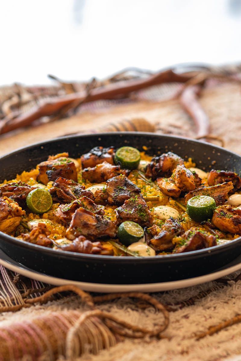 Bowl of spicy roasted vegetables garnished with green pepper slices on a woven mat