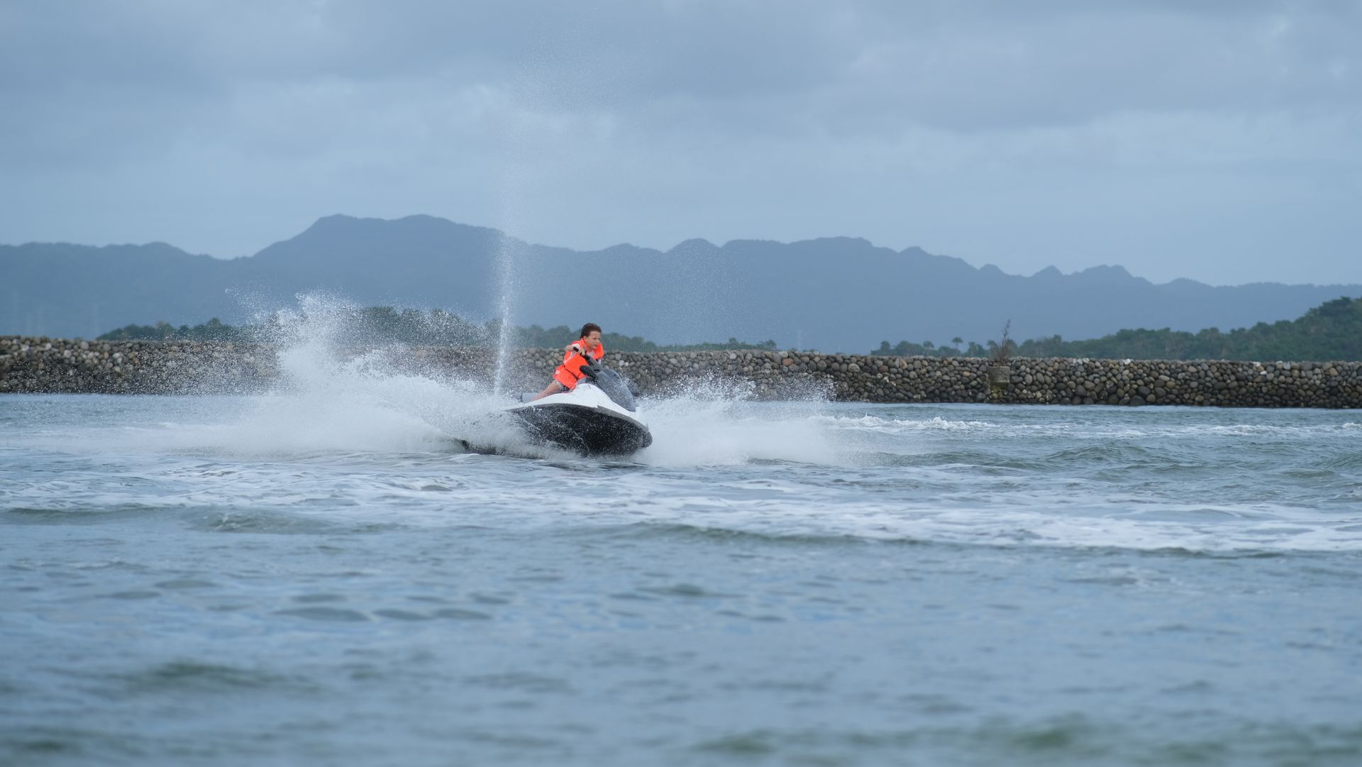 Jet ski racing across choppy water, spraying waves with mountains in the background