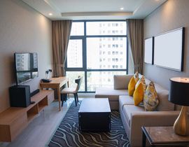 Modern living room with sofa, coffee table, desk, TV, and large window overlooking city buildings