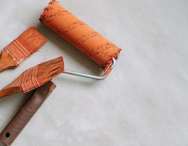 Orange paint roller and brush on a light gray surface