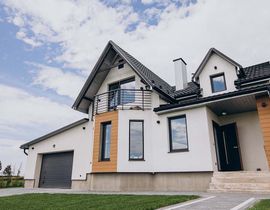 Modern two-story house with a garage, beige exterior, and black roof under a cloudy sky
