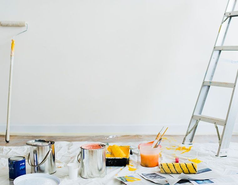Paint supplies and brushes on a drop cloth beside a ladder against a white wall