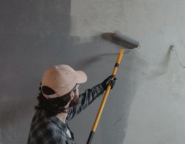 Person painting a gray wall with a roller on a long handle