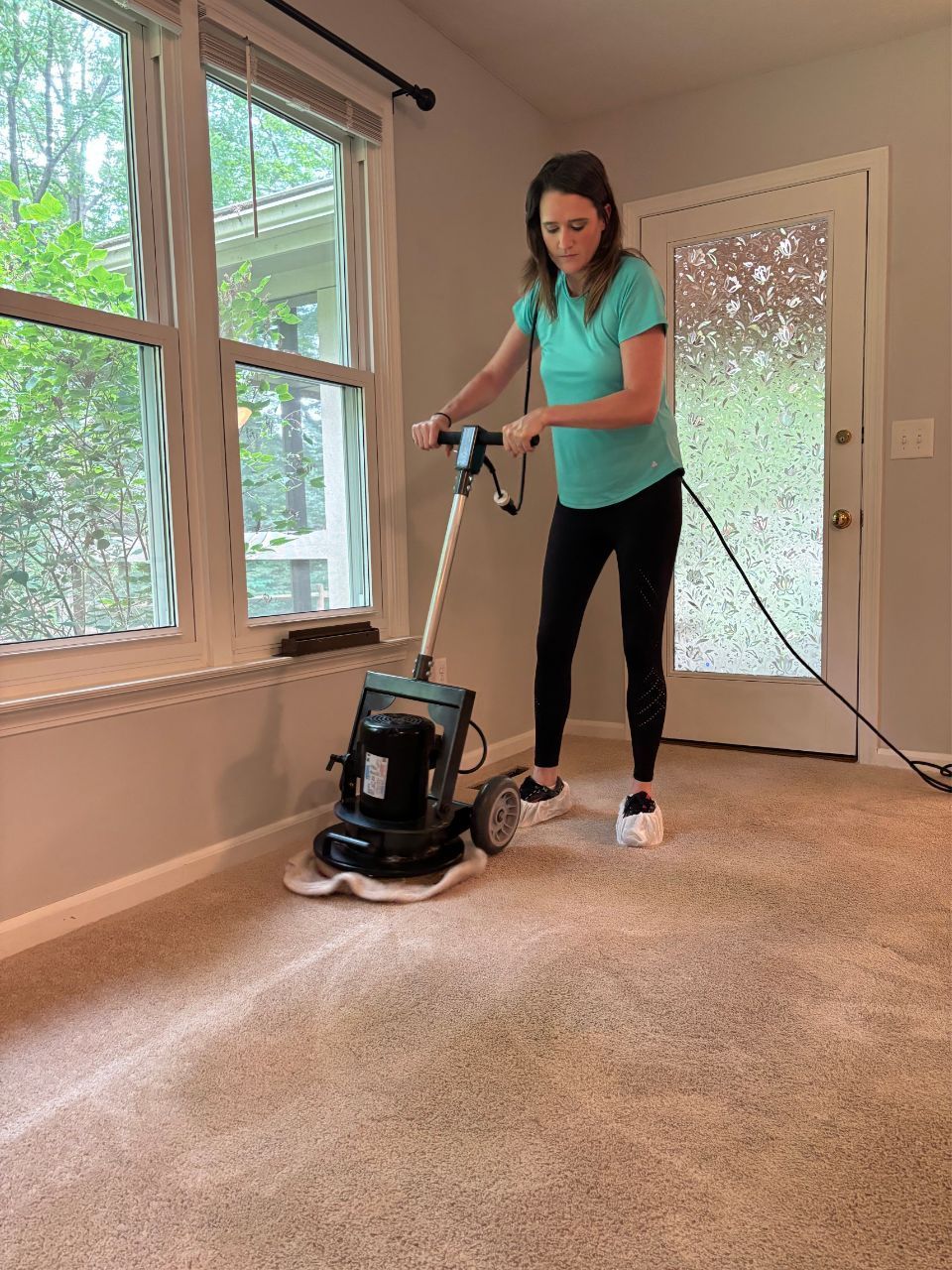 A woman is using a machine to clean a carpet in a living room.