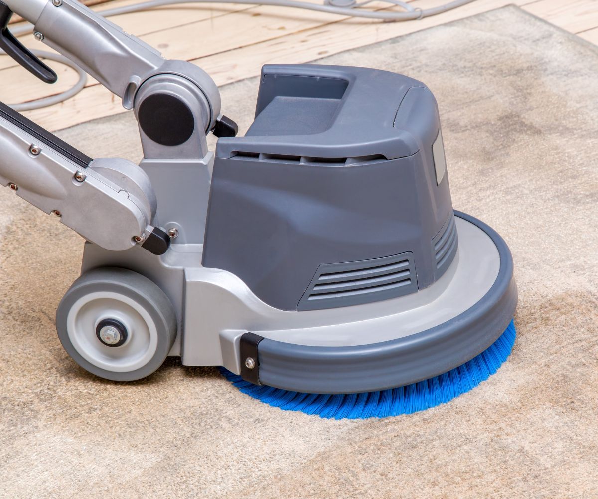 A machine is cleaning a carpet with a blue brush.