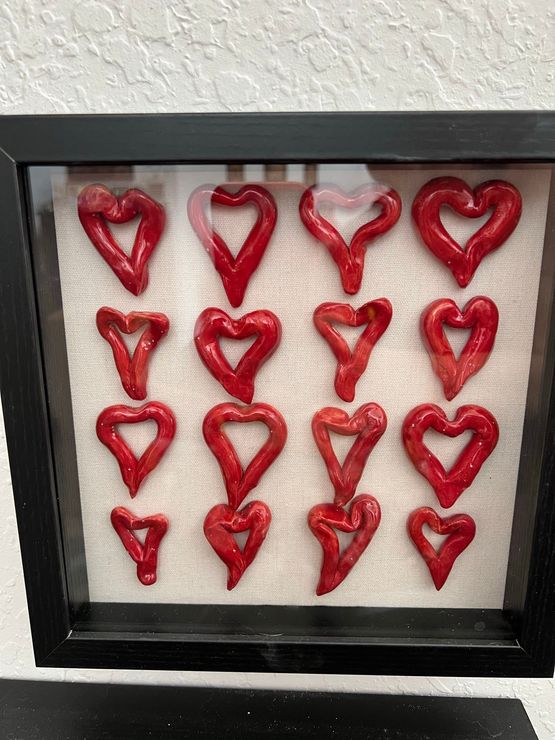 Framed display of red heart-shaped ornaments arranged in a grid on a beige background