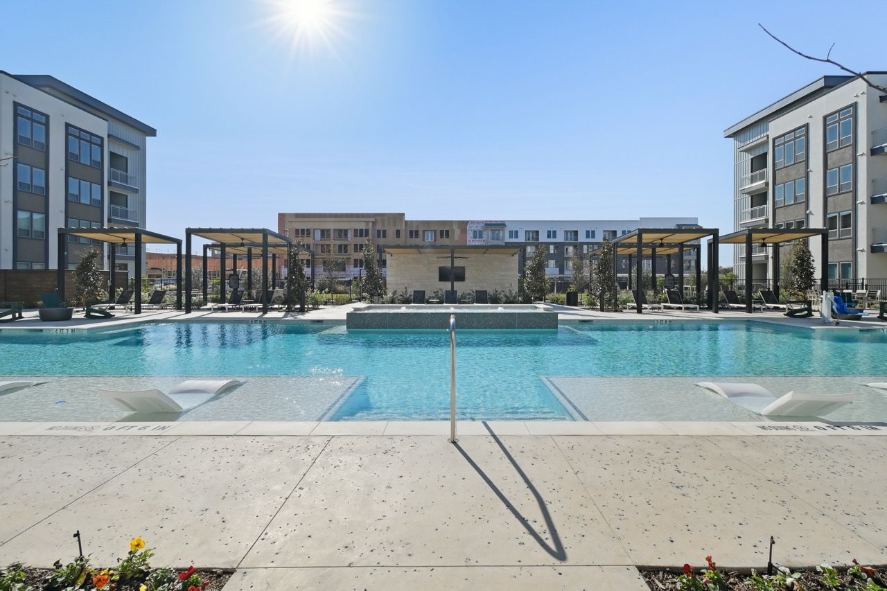 Outdoor apartment community pool with cabanas, lounge chairs, and modern buildings surrounding.