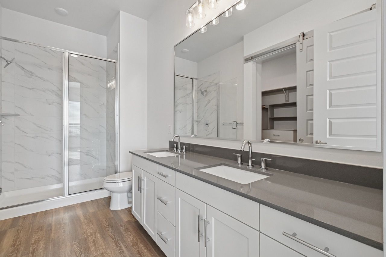 Bathroom with double vanity, gray countertop, glass shower, and marble-tile walls.