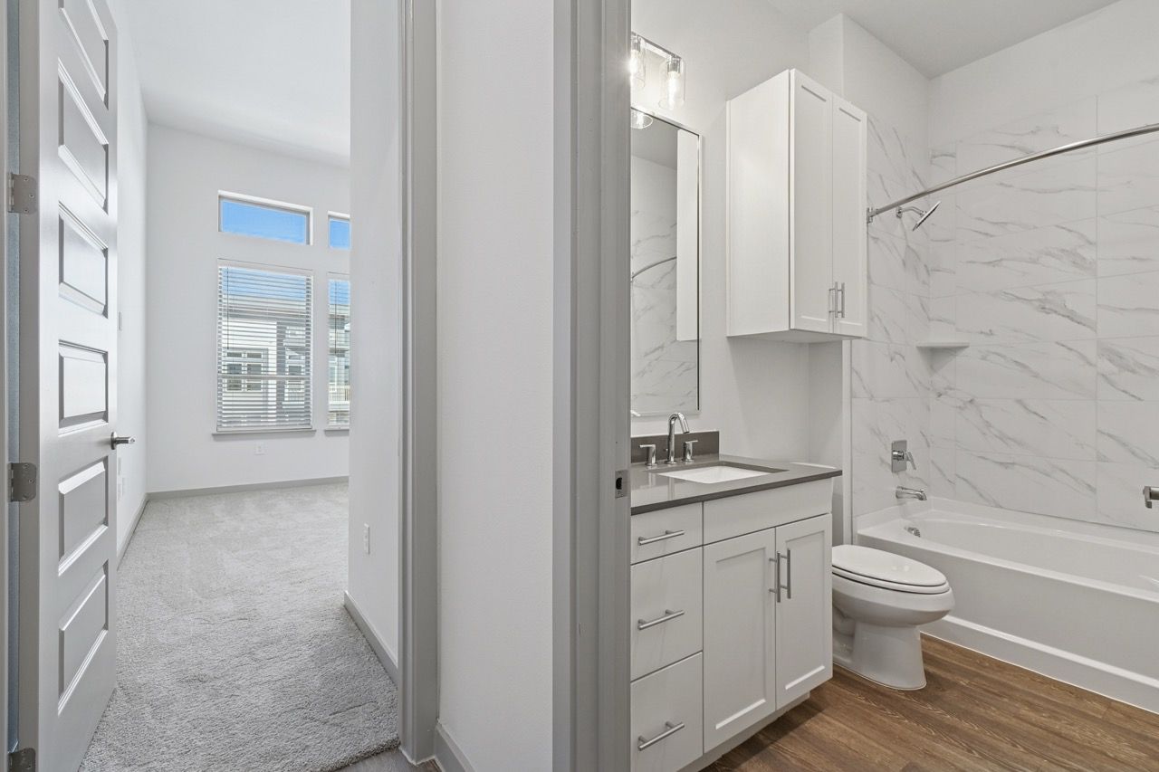 Modern apartment bathroom with marble-tile surround, white vanity, and adjacent carpeted living space.