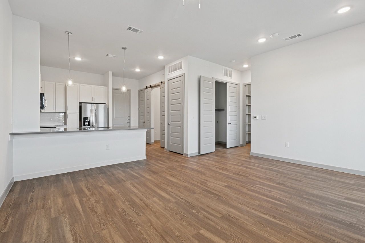 Open-plan kitchen and living area with white cabinets, stainless steel fridge, and wood-look flooring.
