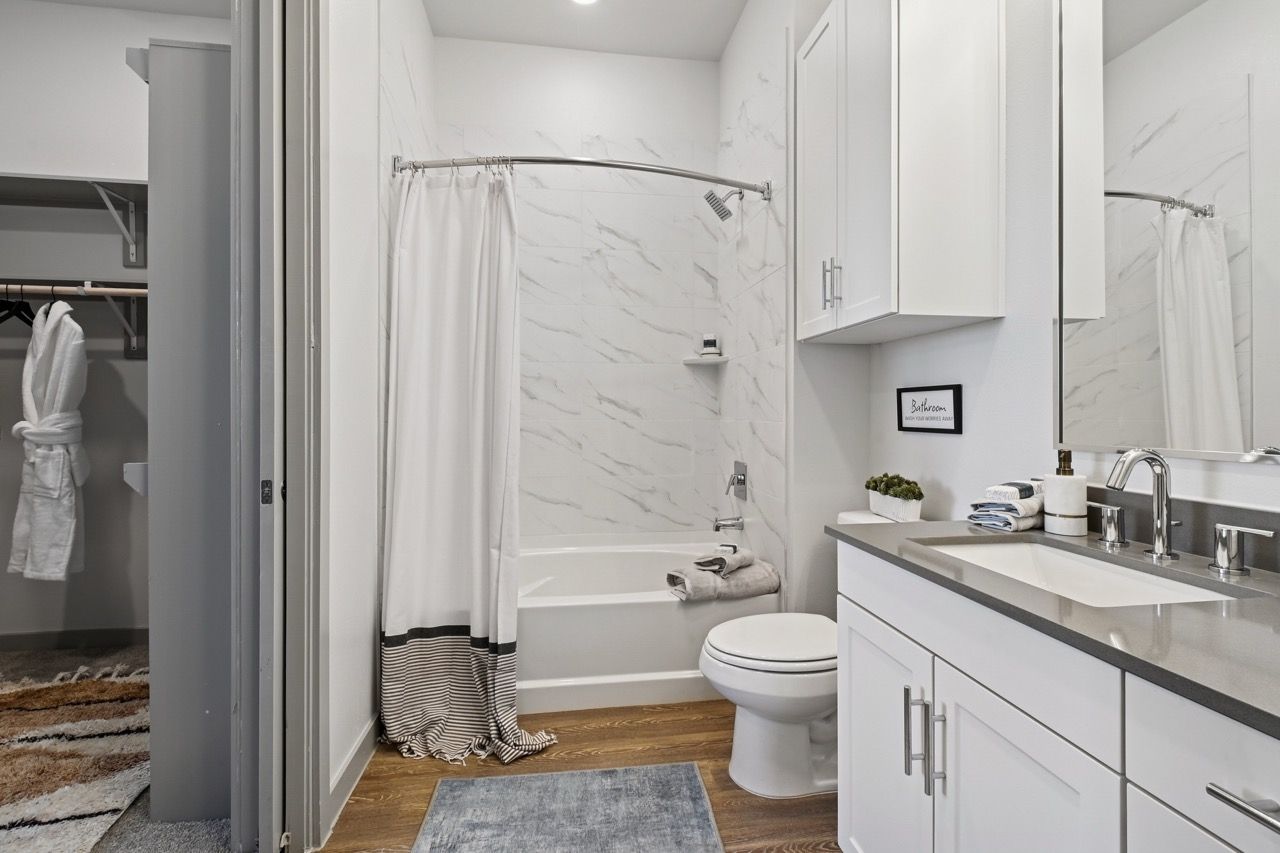 White bathroom with marble-tiled tub/shower, toilet, and white vanity.