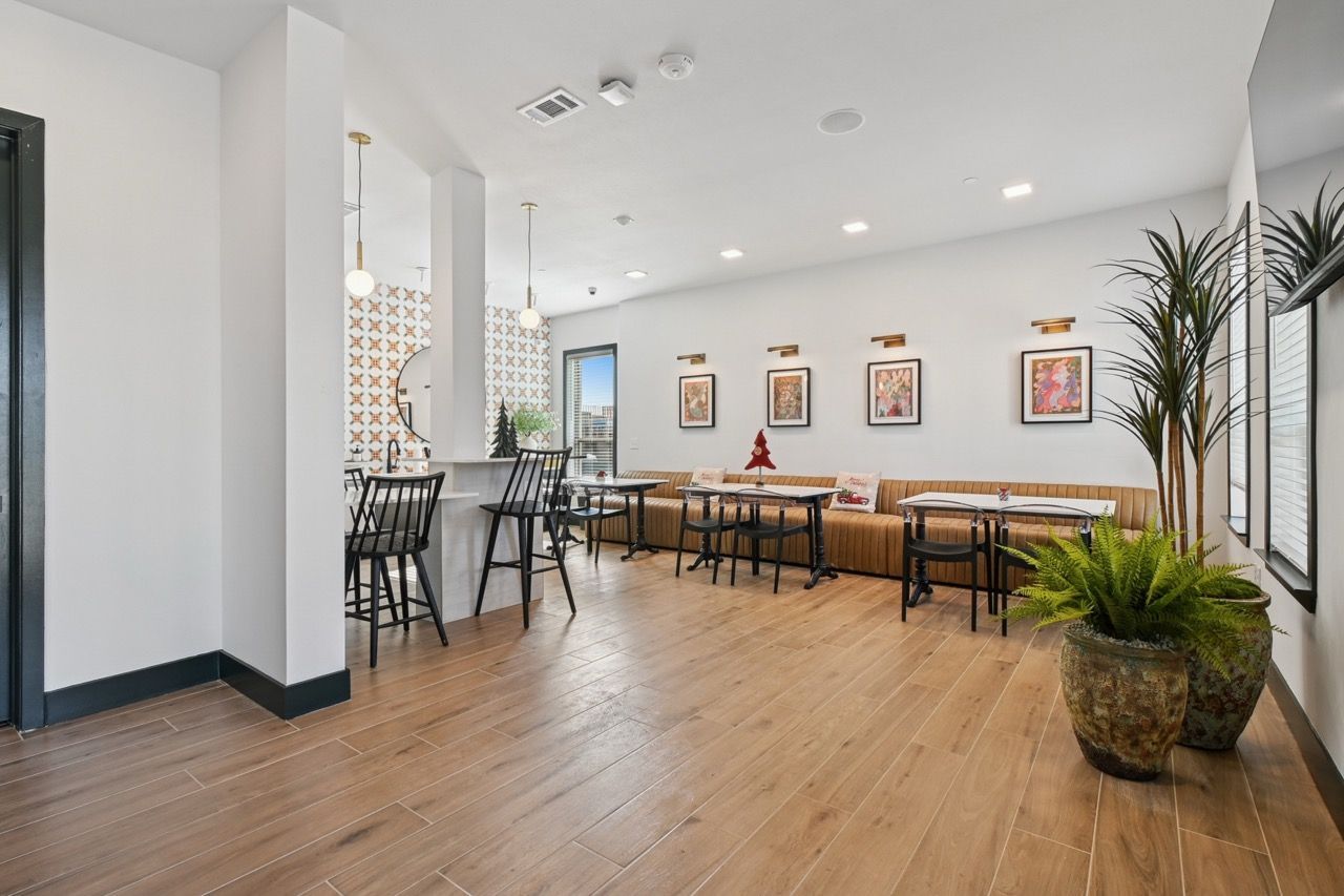 Bright modern resident lounge with a bar counter, high chairs, tables, and large potted plants.