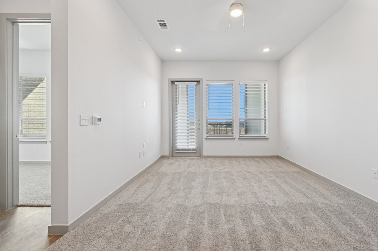 Unfurnished living room with white walls, beige carpet, blinds, and a balcony door.