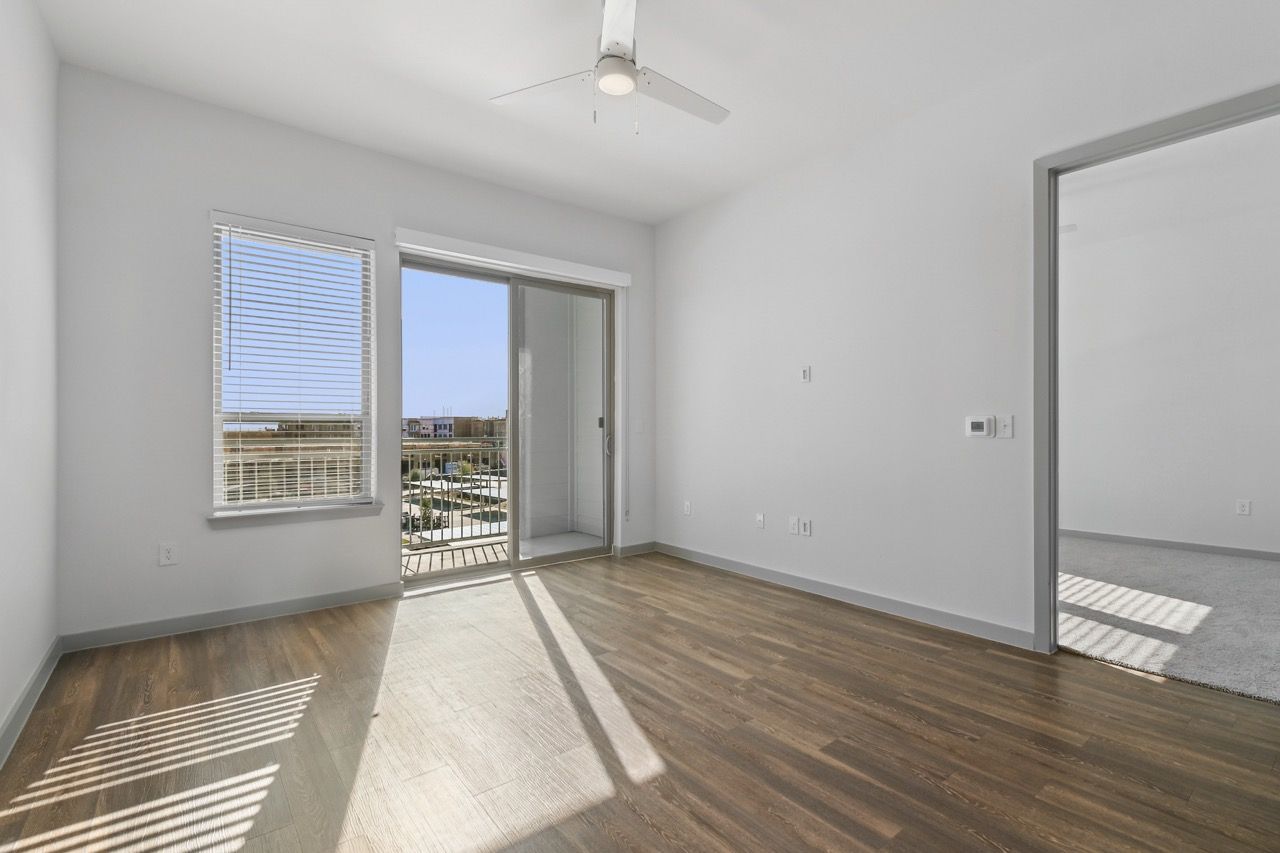 Empty living room with wood-look flooring, ceiling fan, and sliding door to balcony.
