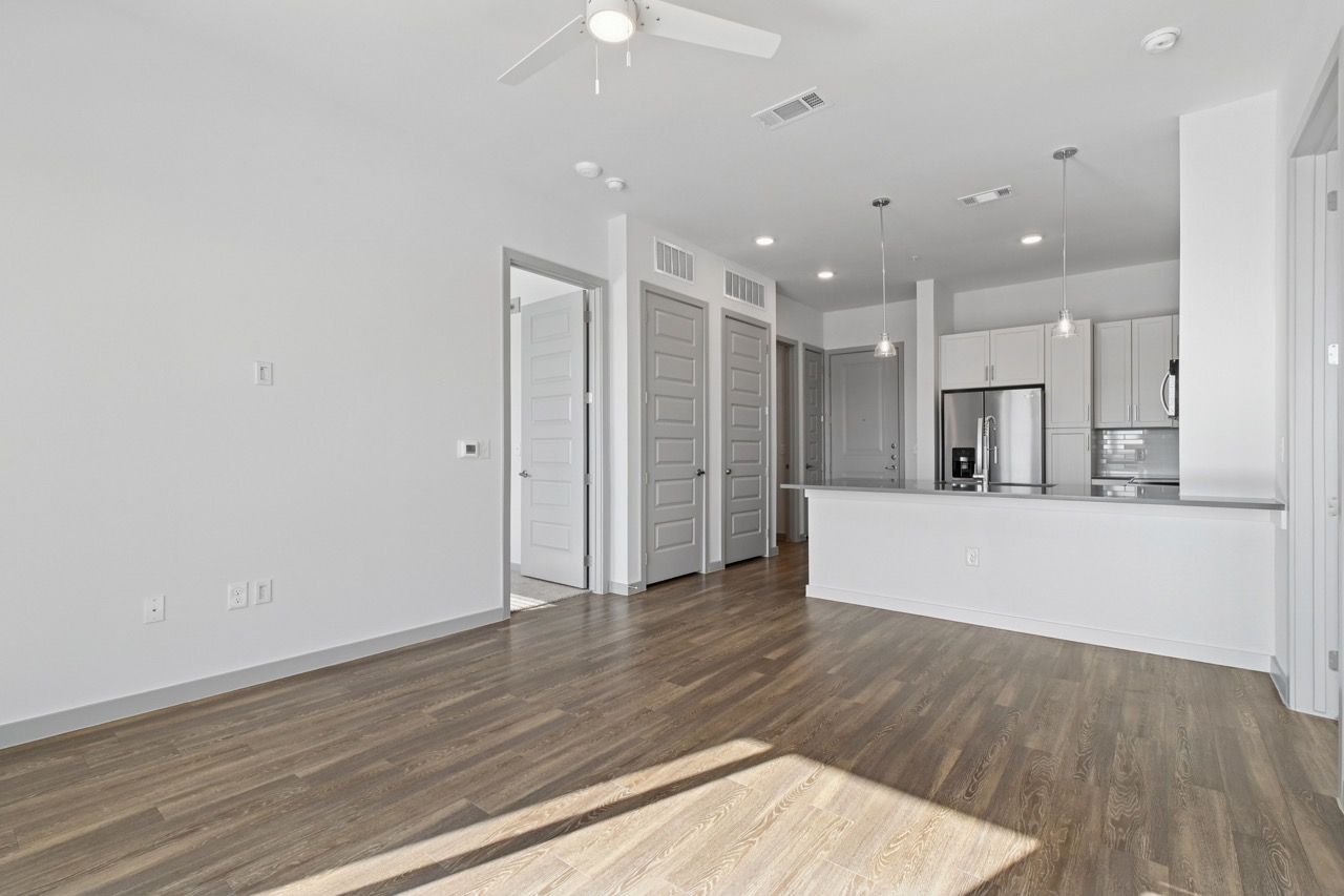 Open living area with hardwood floors, white walls, and a modern kitchen with an island.