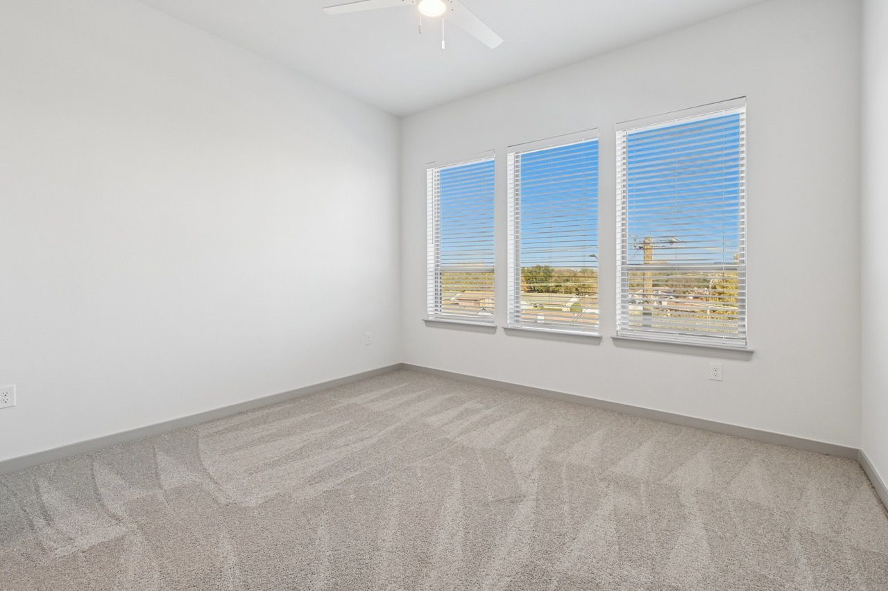 Empty carpeted bedroom with three windows and blinds.