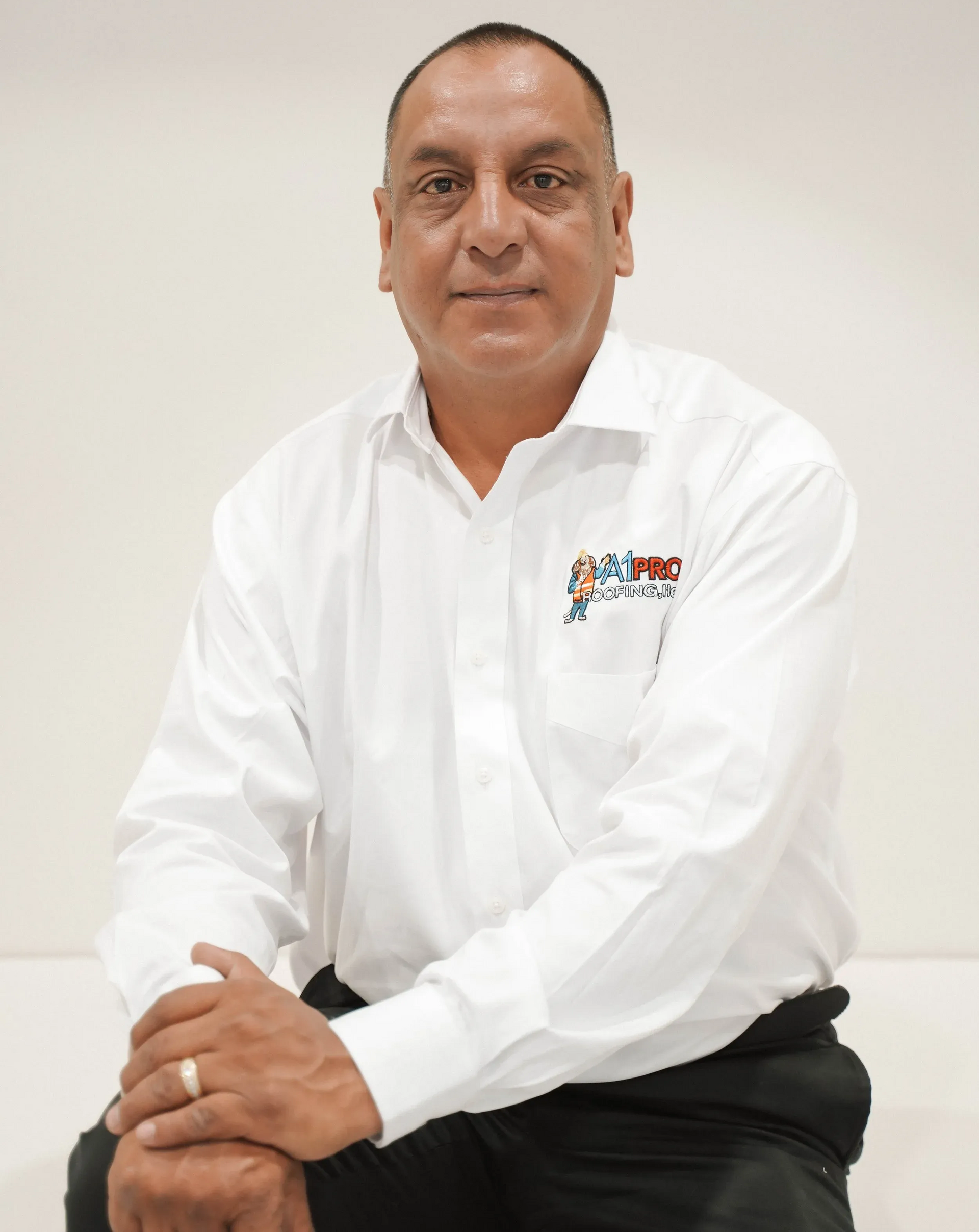 A person wearing a white button-down shirt with a small logo on the chest, sitting against a plain white background.