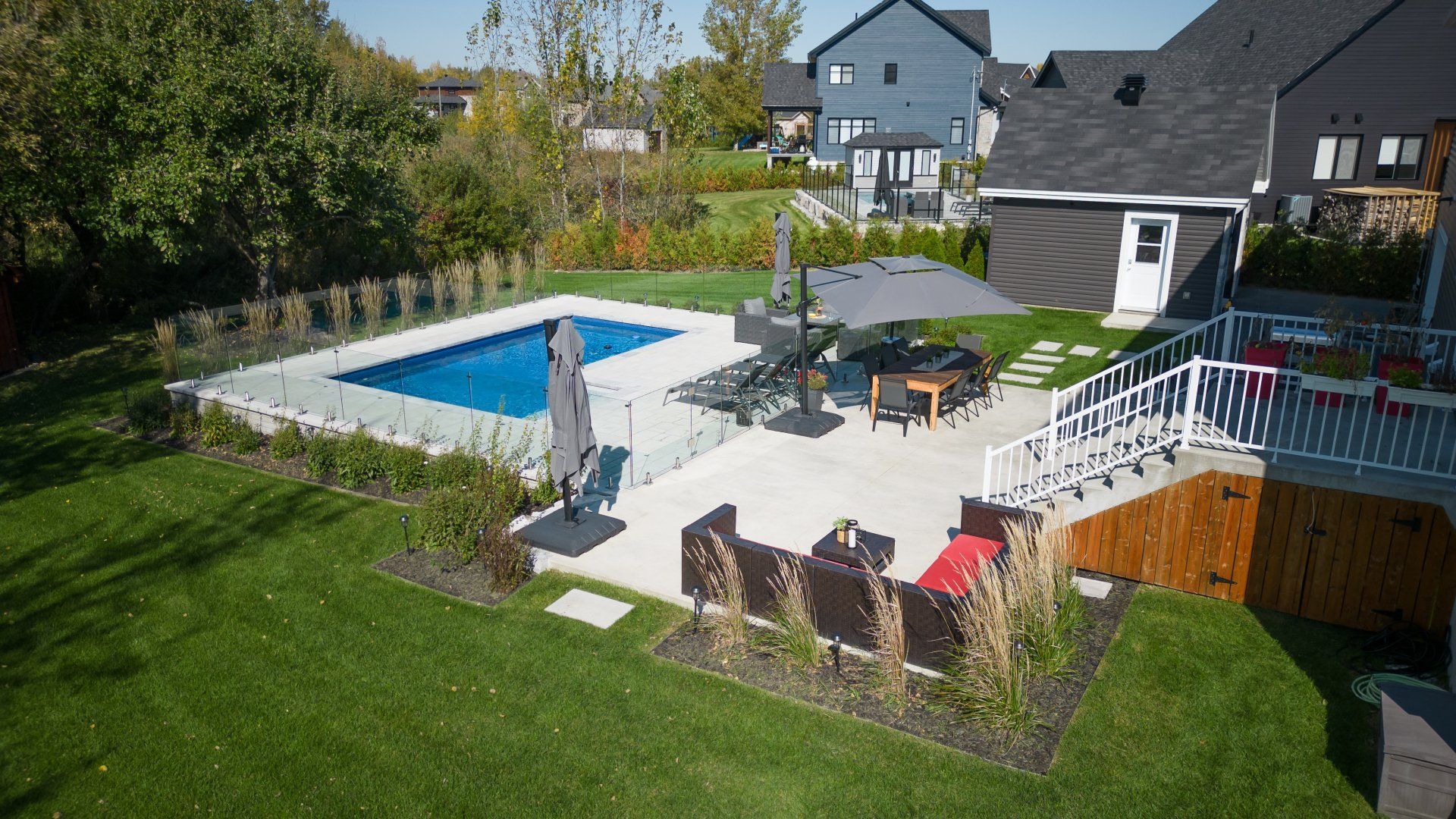 Le jardin arrière comprend une piscine avec une clôture en verre, un ensemble de patio avec un parasol gris et des canapés d'extérieur.