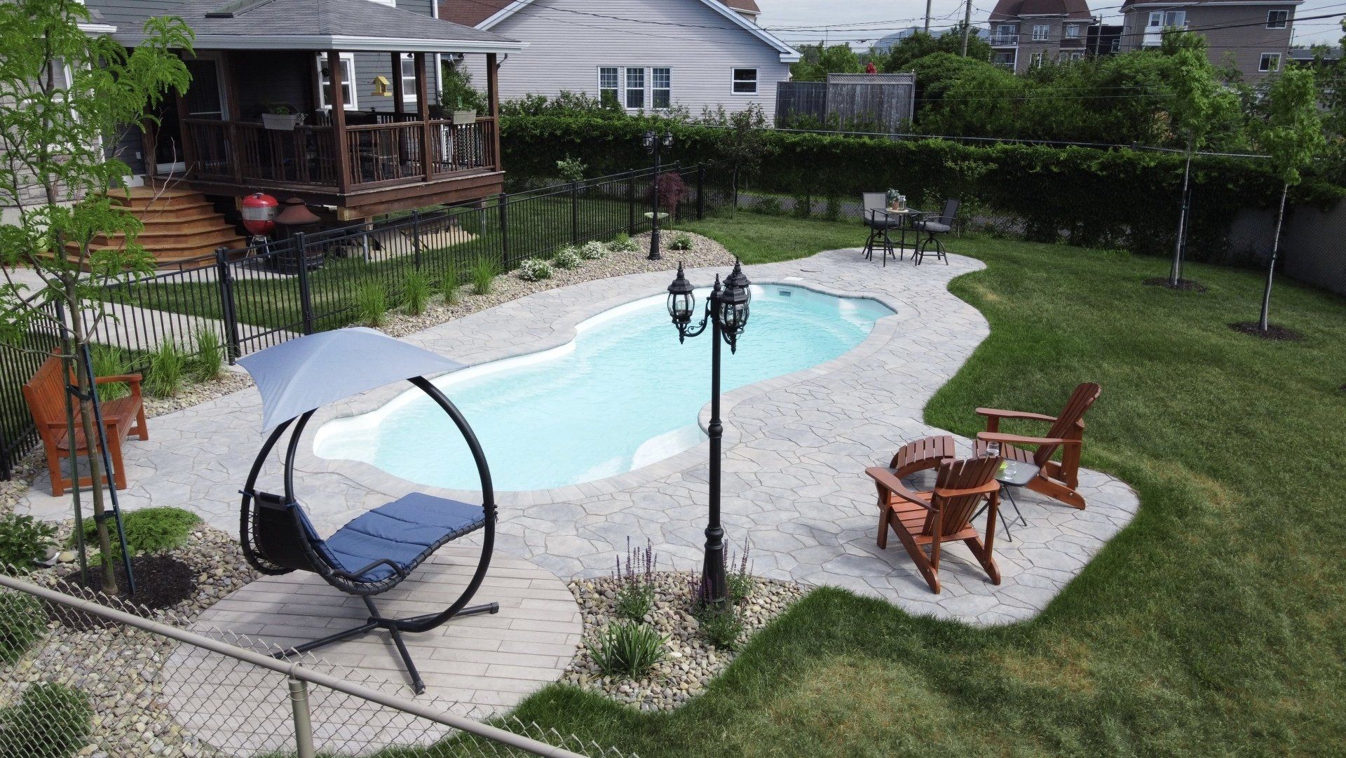 Vue en plongée d'un jardin avec piscine, parasol, allée en pierre et sauna tonneau sur une terrasse.