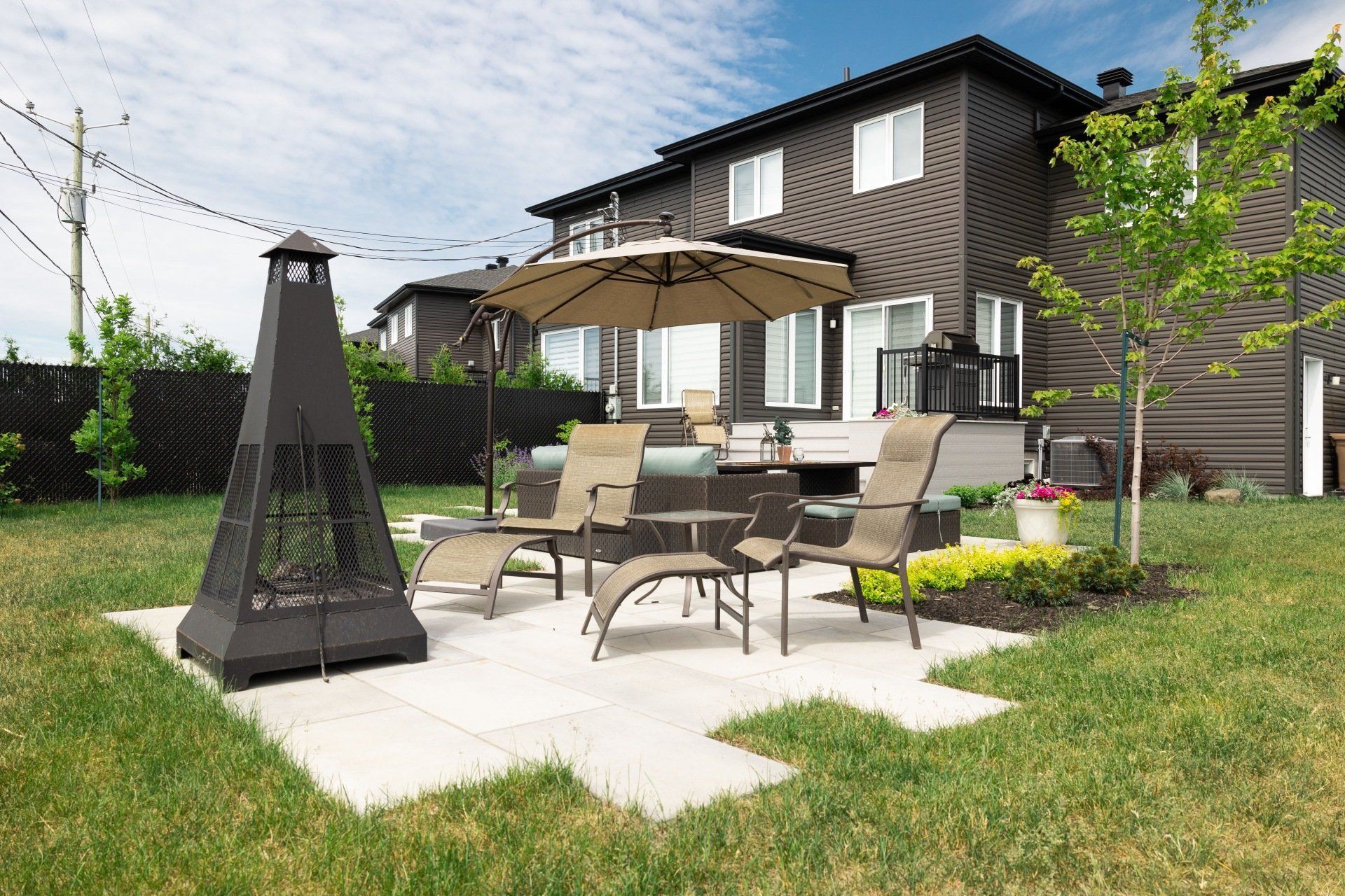 Une terrasse avec un foyer, des chaises Adirondack et un banc en pierre dans une cour arrière, agrémentée d'un mur de soutènement en pierre et de gazon.