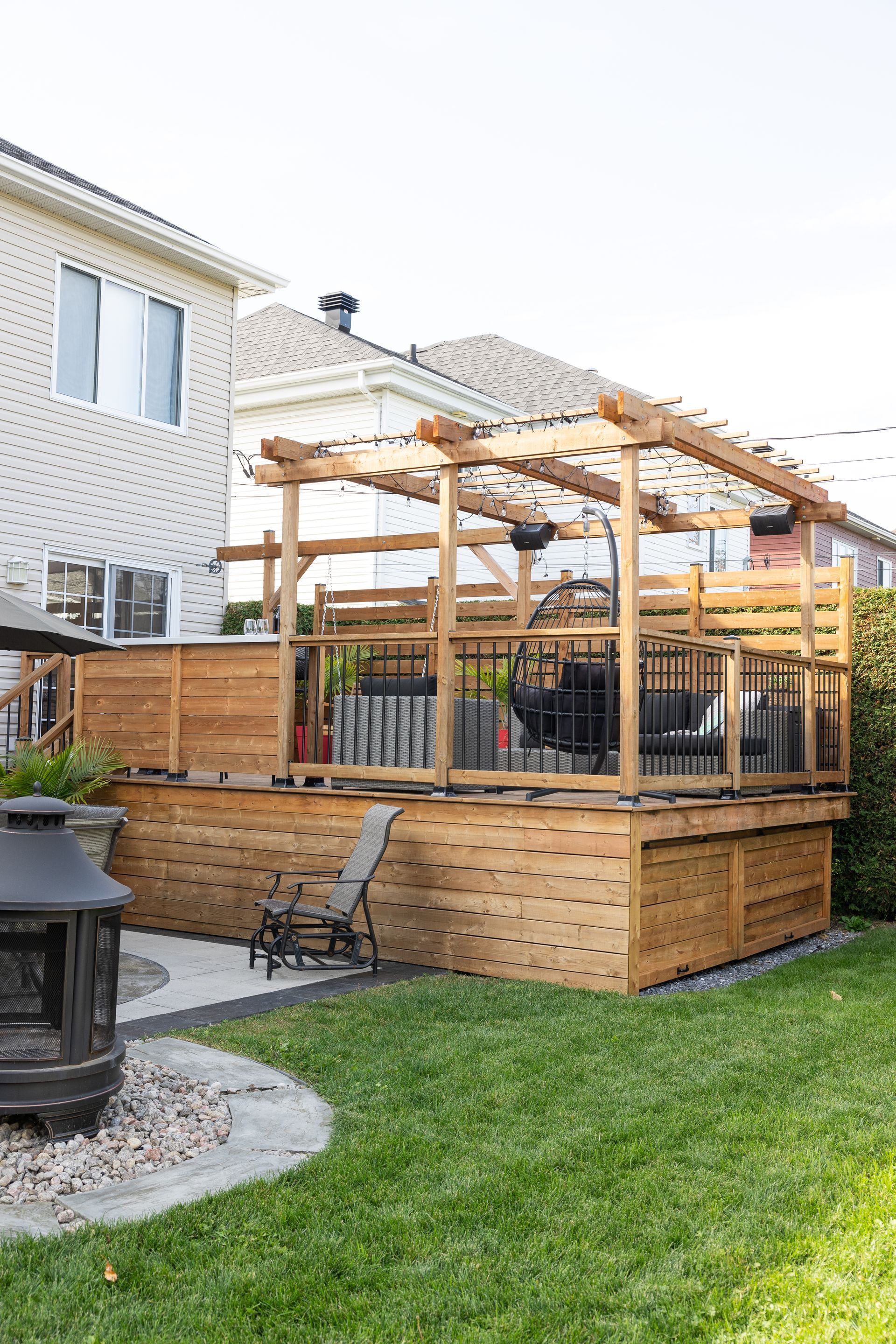 Une terrasse en bois avec une pergola et des panneaux d'intimité se trouve dans une cour arrière jouxtant une maison au revêtement extérieur clair.