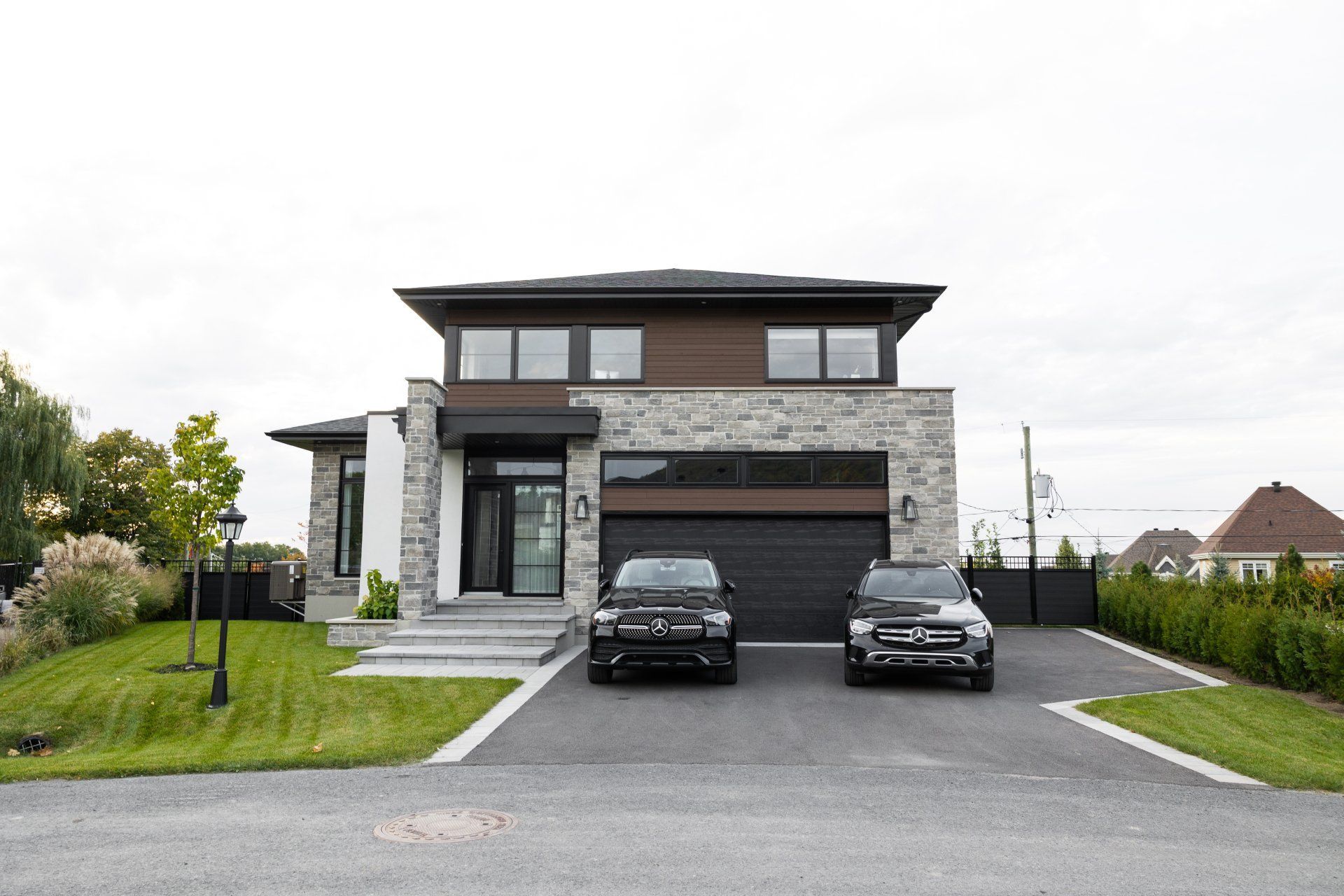 Maison de banlieue moderne de deux étages avec façade en pierre, garage double et allée asphaltée pouvant accueillir deux voitures.