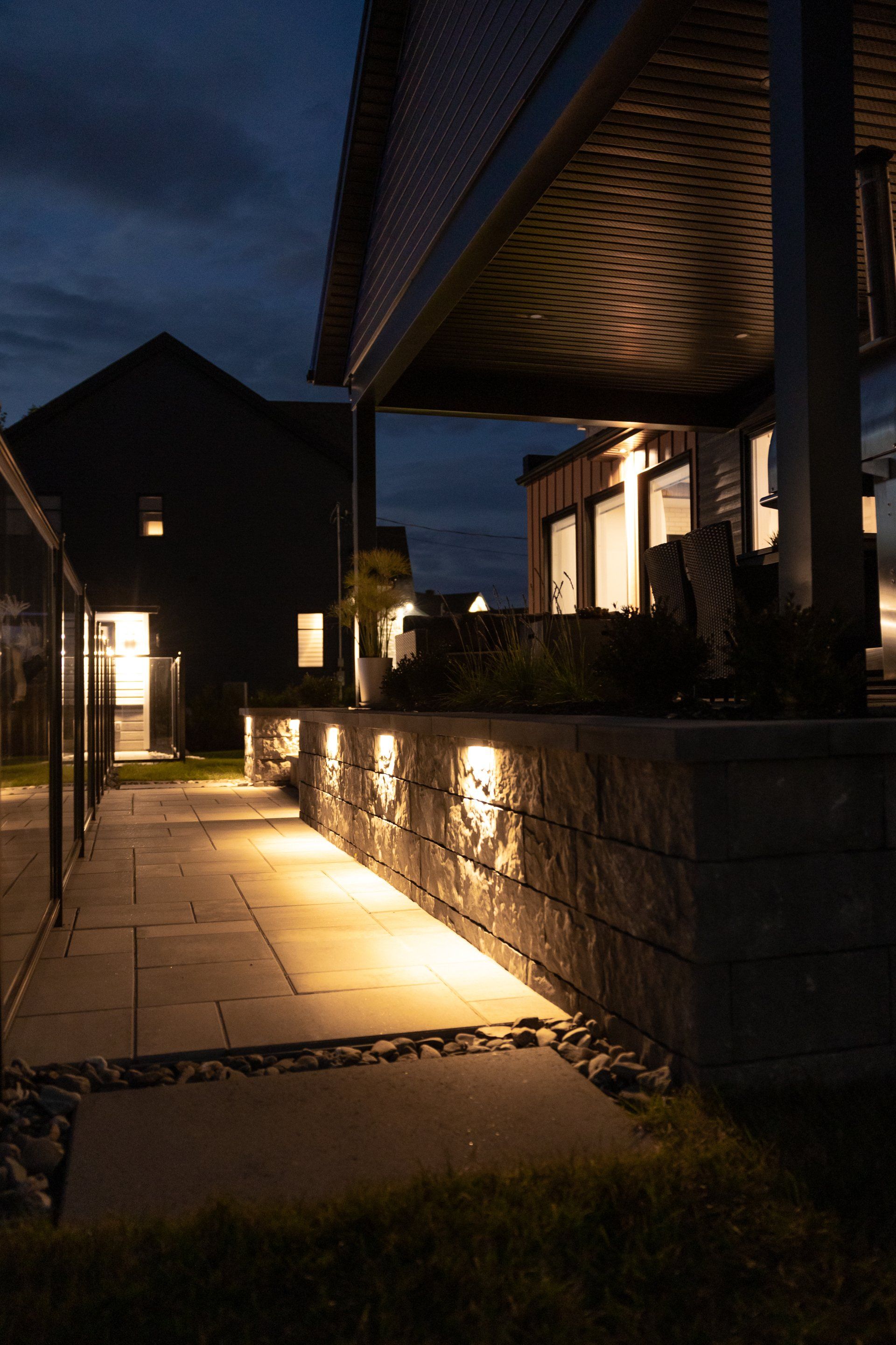 Au crépuscule, un muret et une allée en pierre illuminés diffusent une douce lumière sur les pavés.