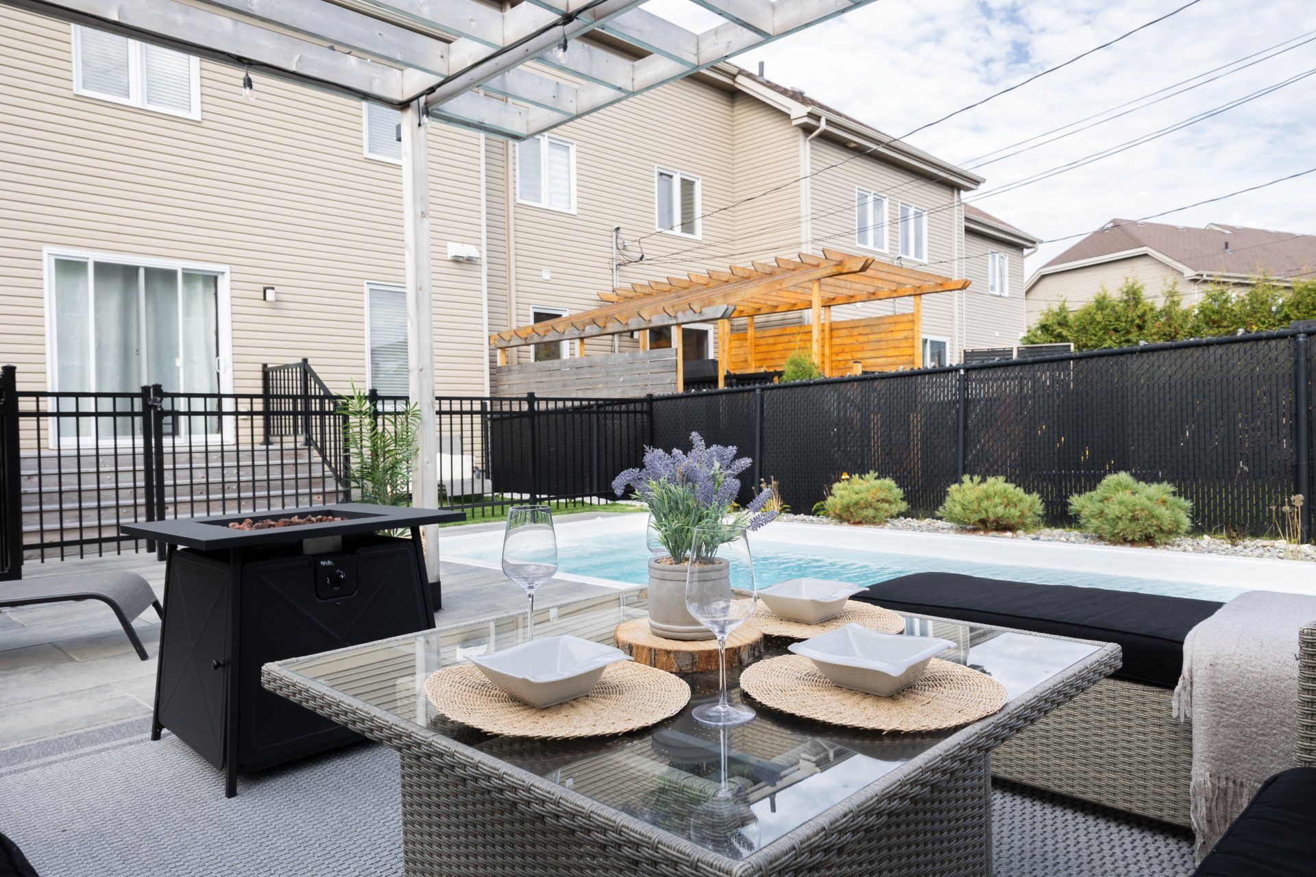 Deux chaises longues et une petite table sous un grand parasol beige déporté sur une terrasse ensoleillée au bord d'une piscine.