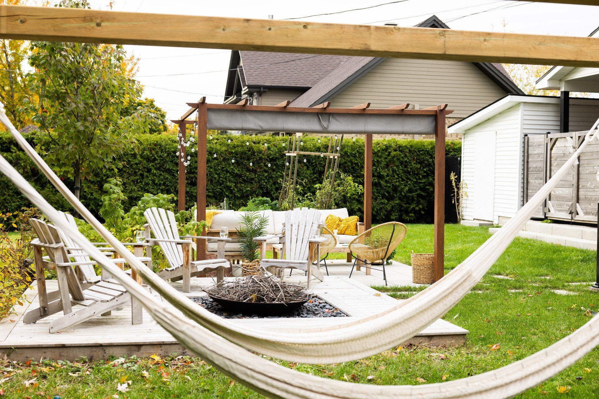 Un ensemble de patio avec des chaises Adirondack blanches et une pergola, vu depuis un hamac dans un jardin de banlieue.