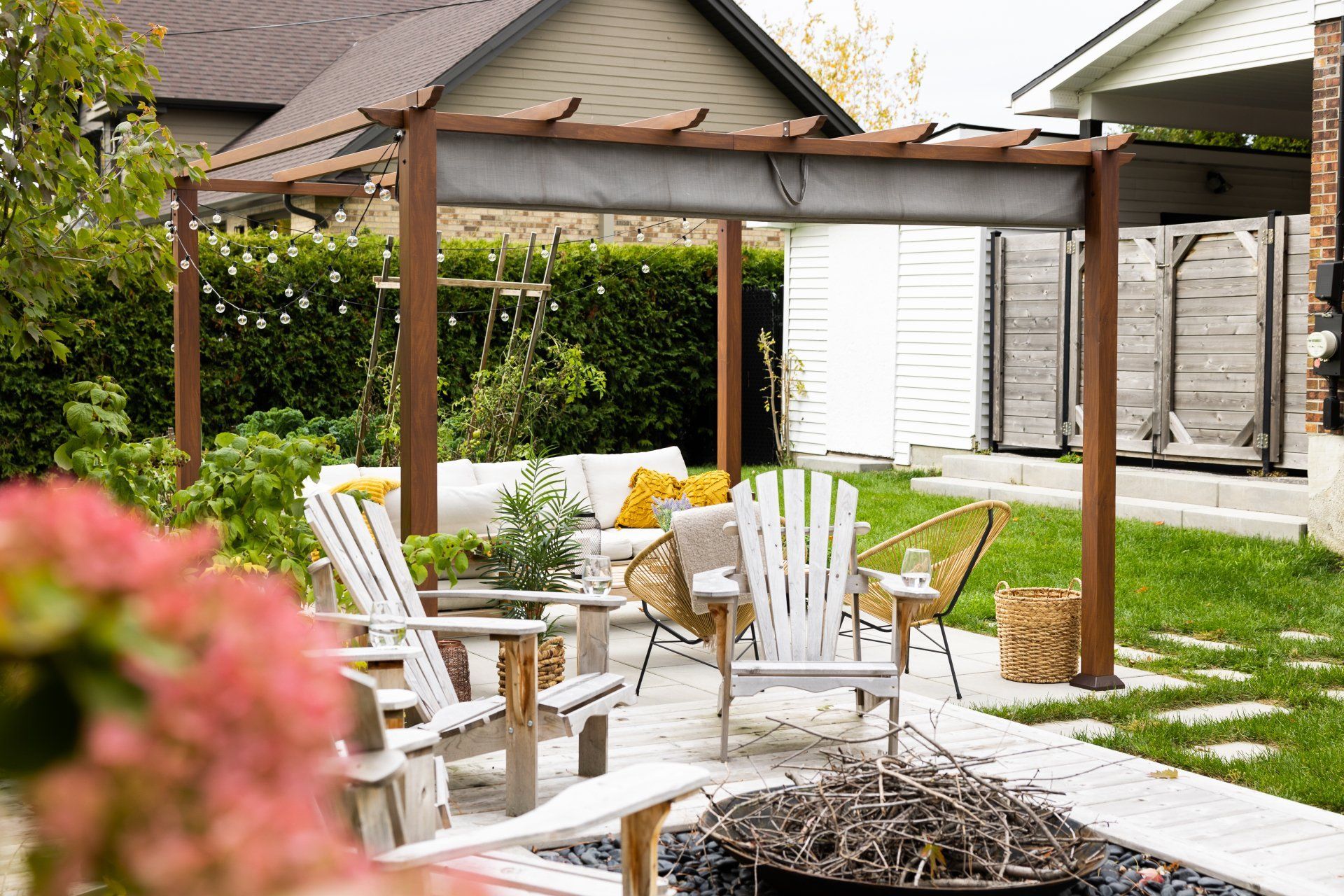 Une terrasse arrière avec une pergola en bois, des chaises Adirondack, un canapé d'extérieur et un foyer sur une surface en pierre.