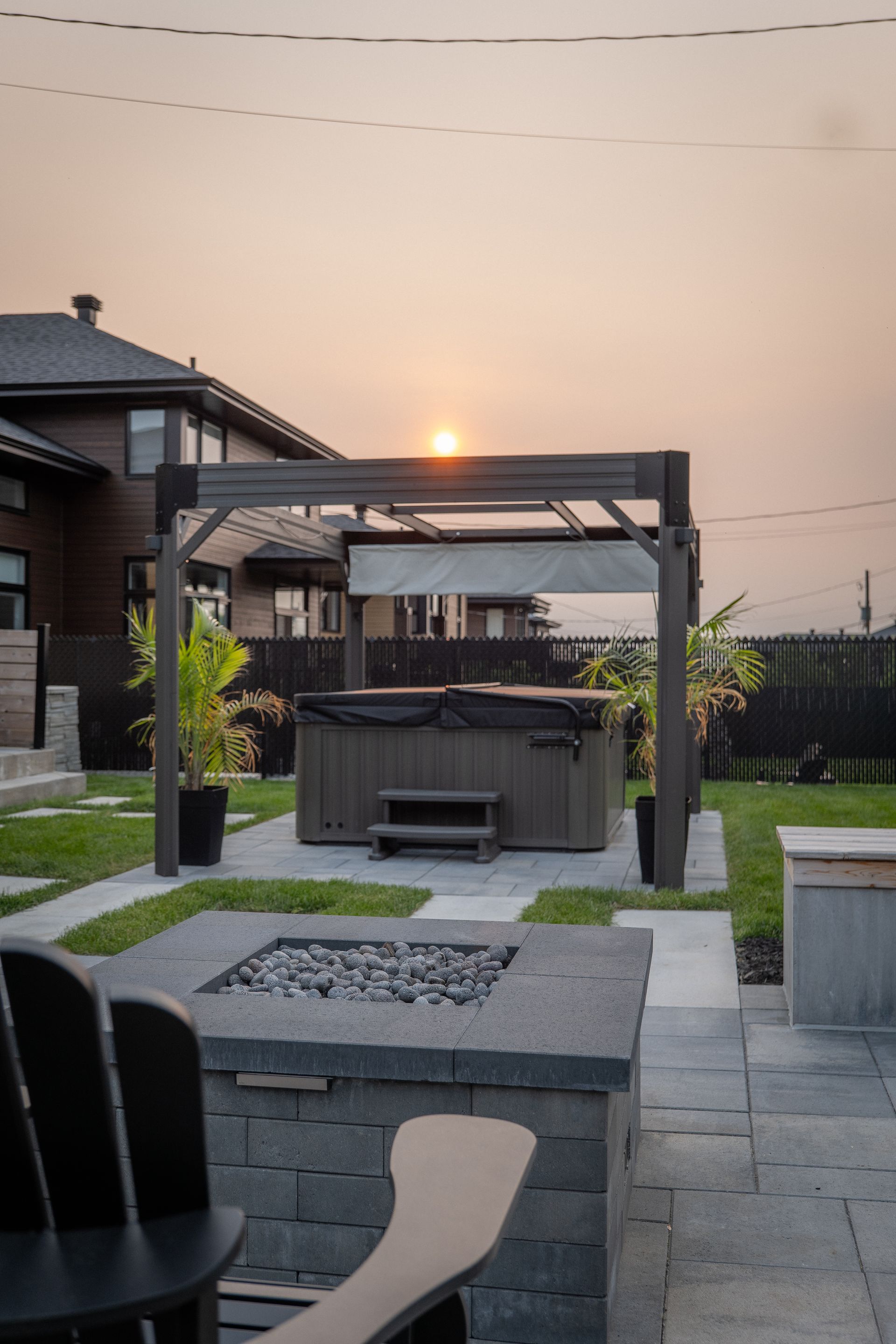 Un espace piscine dans le jardin comprenant une piscine bleu clair, un transat suspendu, des sièges en bois et une maison avec une terrasse.