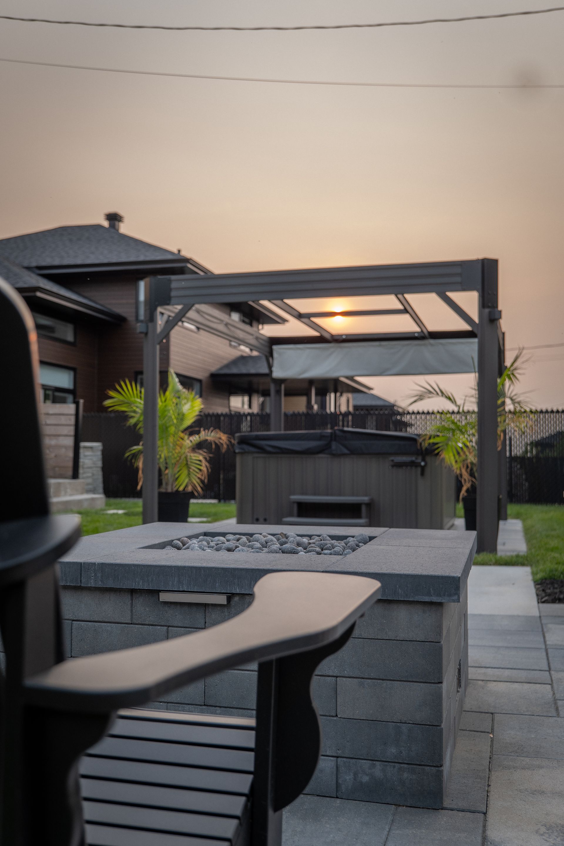 Une cuisine extérieure avec un îlot revêtu de pierre, un barbecue en acier inoxydable et des sièges de bar sous un pavillon en bois.