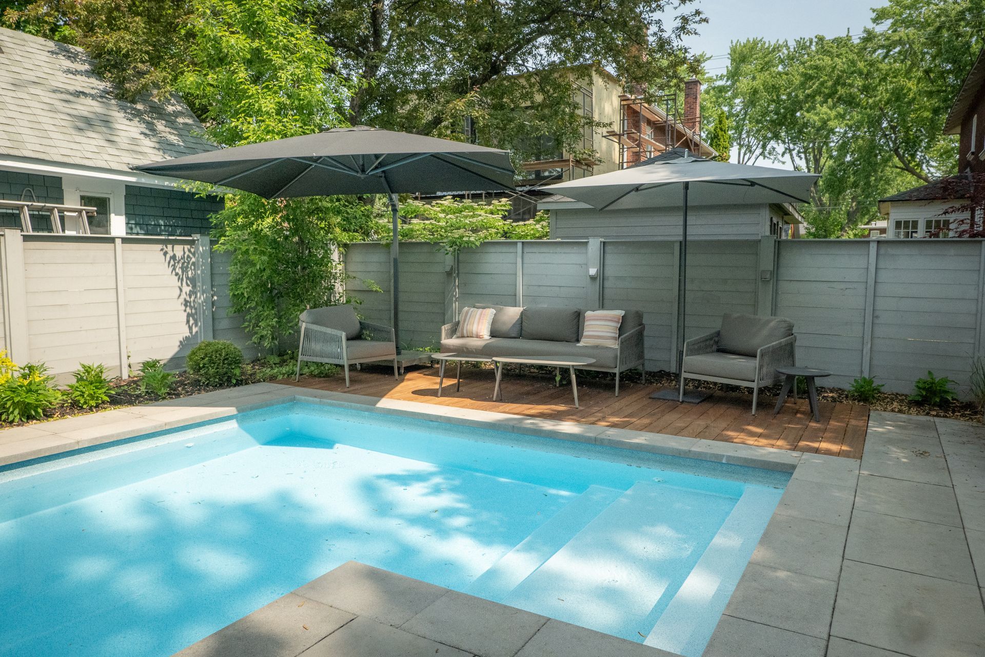 Une terrasse arrière avec des chaises sombres et du mobilier de jardin jouxte une maison en pierre et en bois dotée d'une terrasse surélevée.