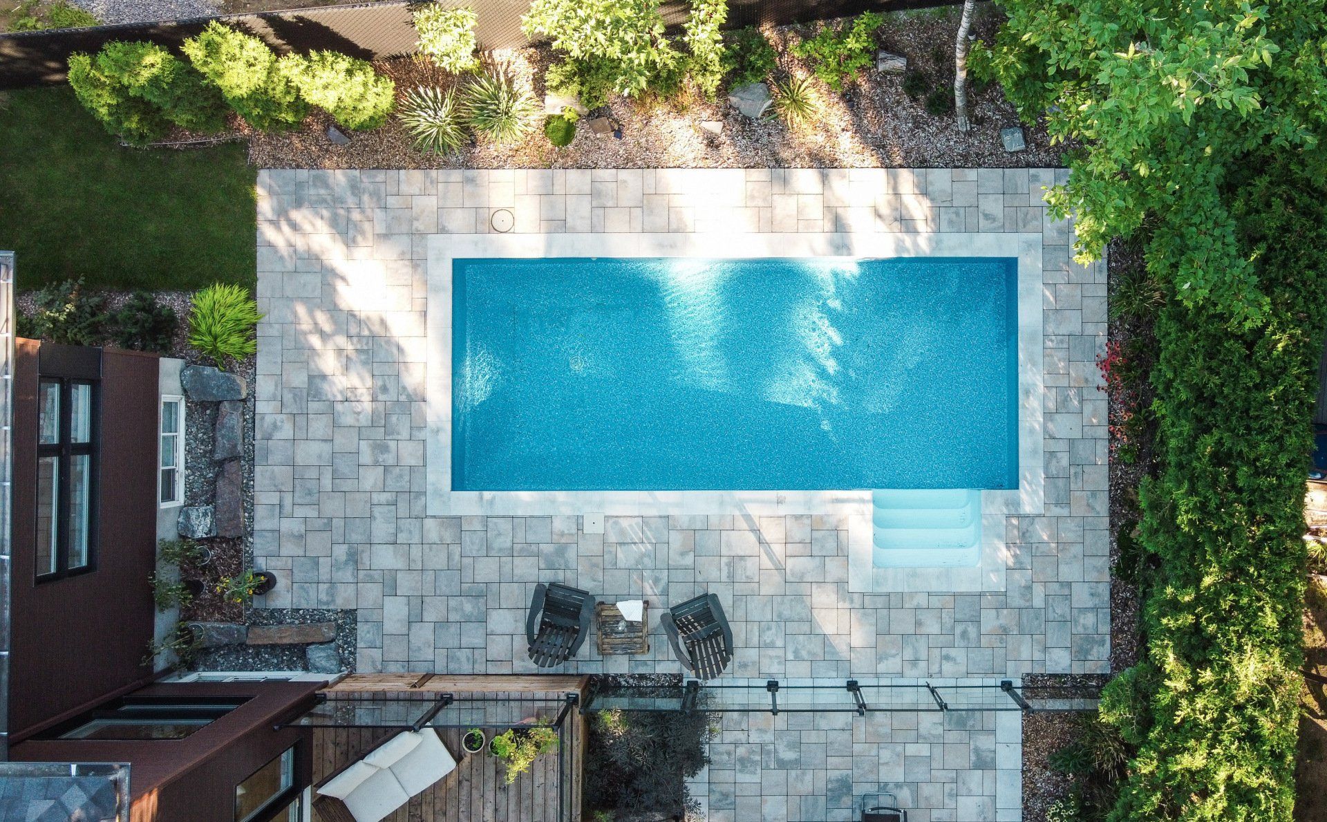 Vue aérienne d'une piscine rectangulaire d'un bleu éclatant, entourée d'une terrasse en pierre claire et d'une végétation luxuriante.