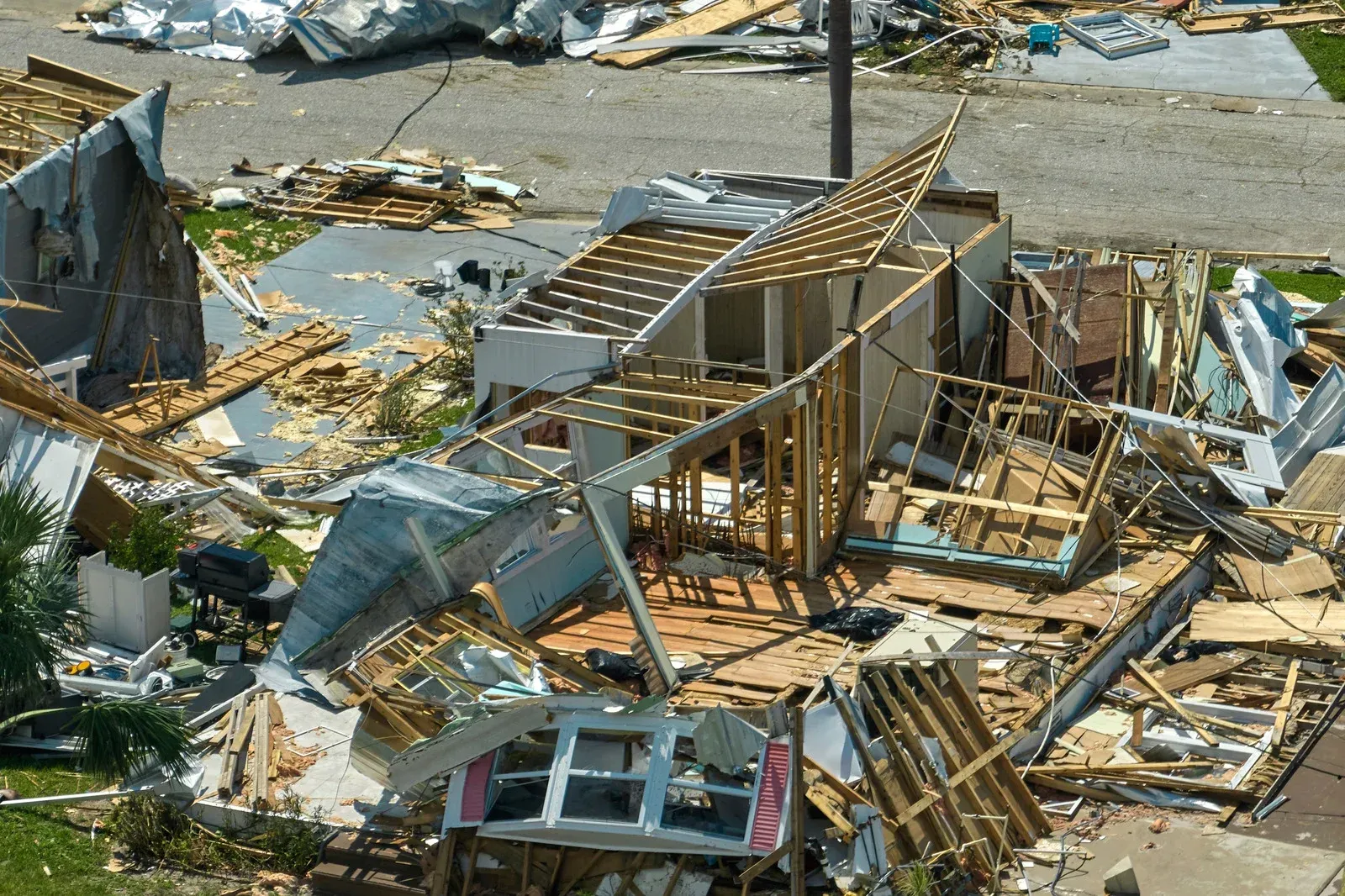 Debris from a destroyed house after a hurricane; wood framing, siding, and roof scattered.