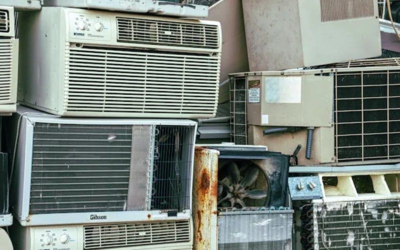 A pile of old air conditioners are stacked on top of each other.
