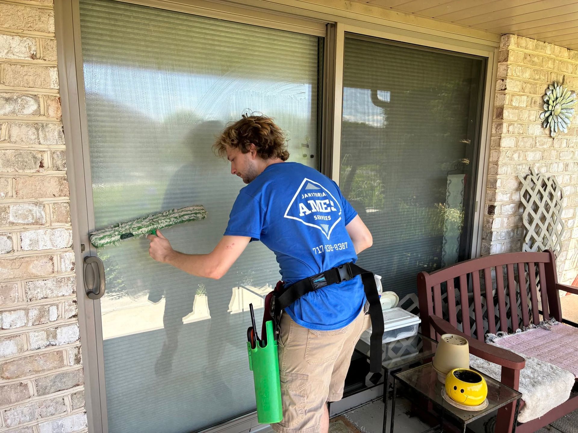 Person cleaning a glass patio door with a squeegee on a covered porch