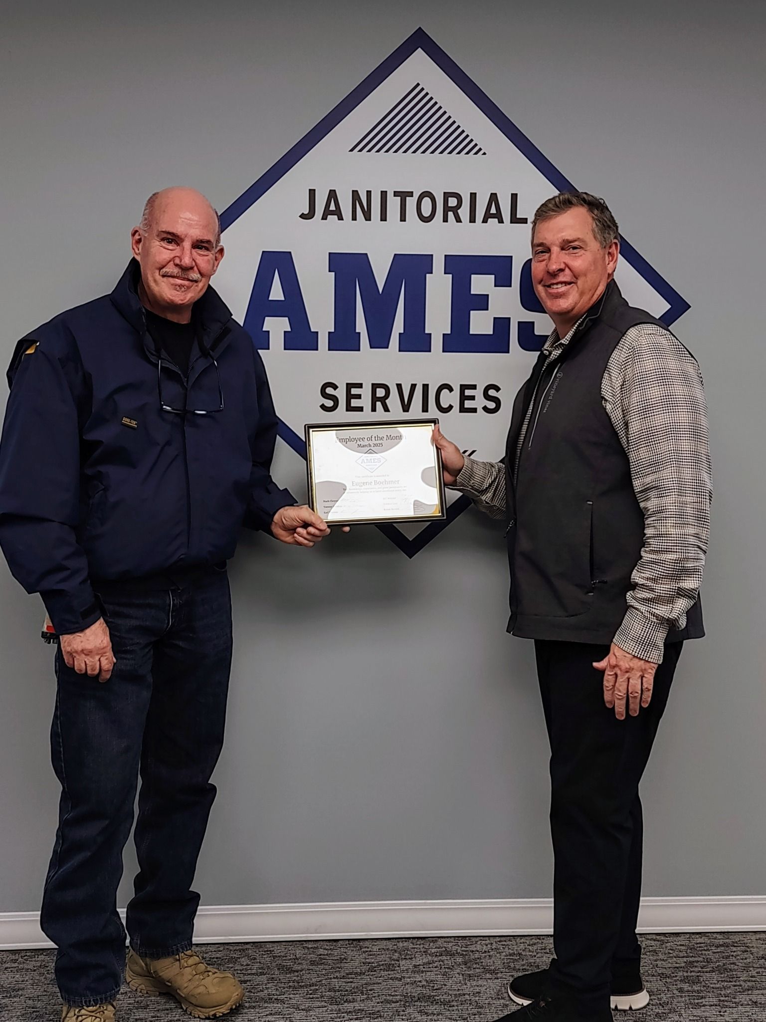 Two men holding a framed certificate in front of a 
