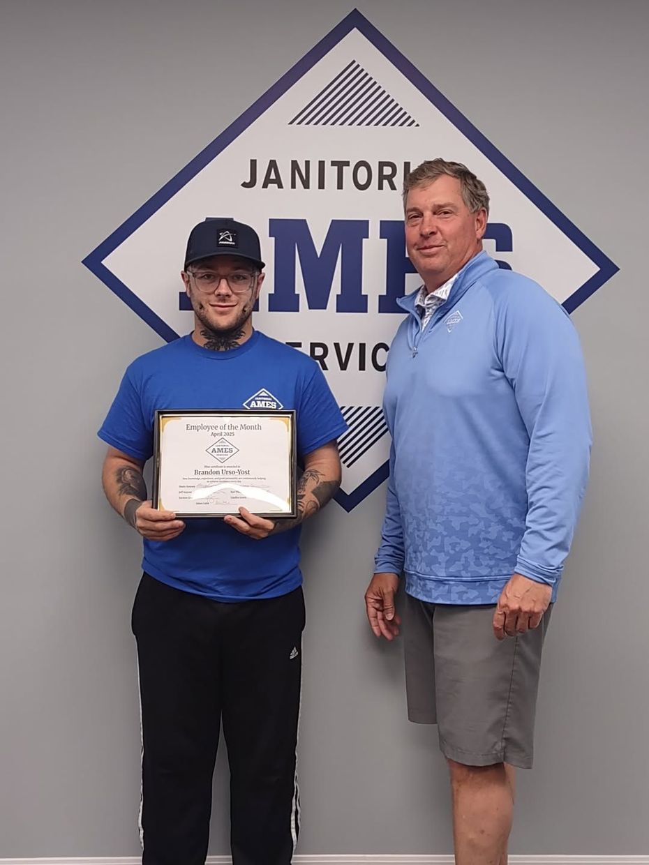Two men standing in front of a logo; one holds a certificate. 