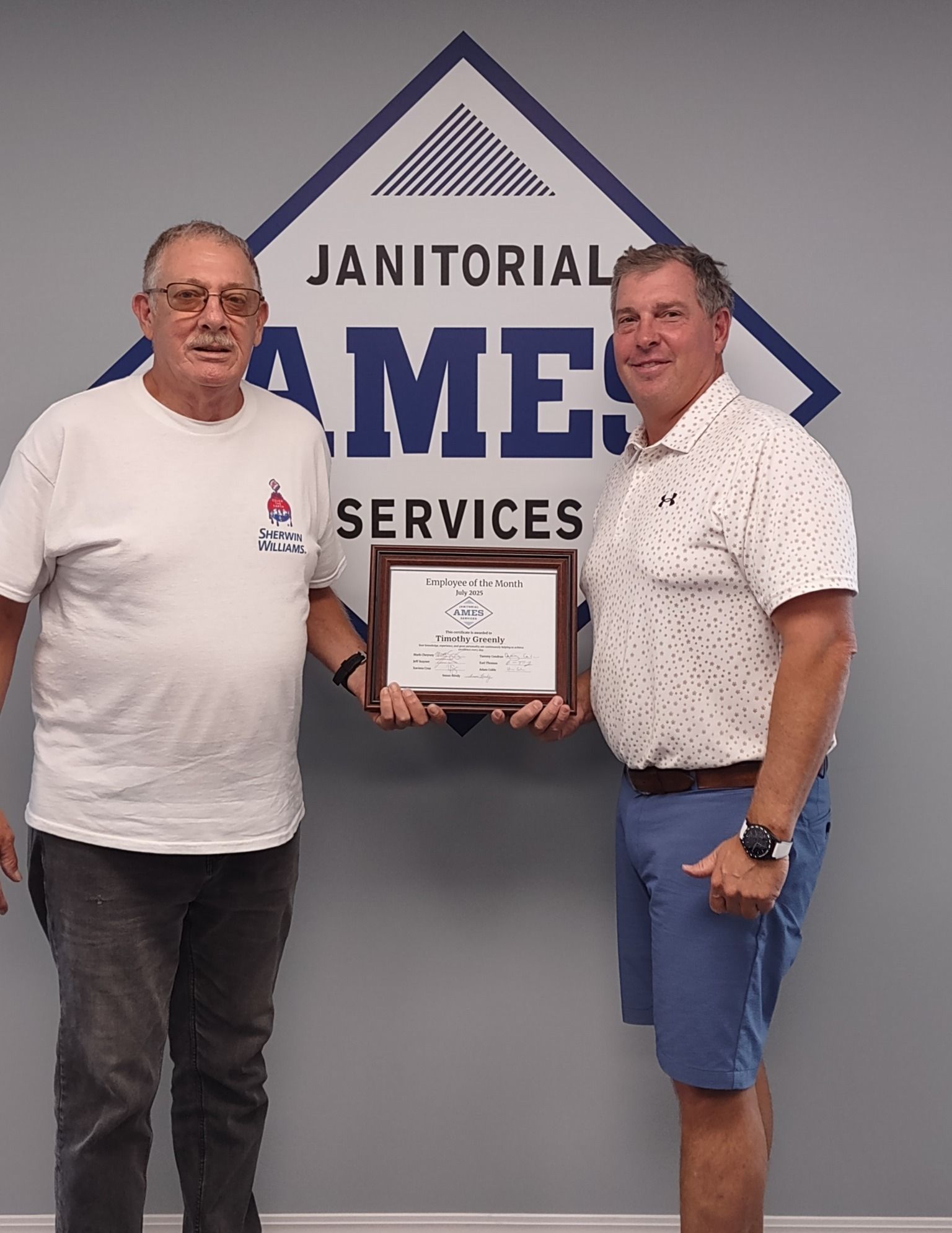 Two men holding a framed award in front of a Janitorial Services logo. 