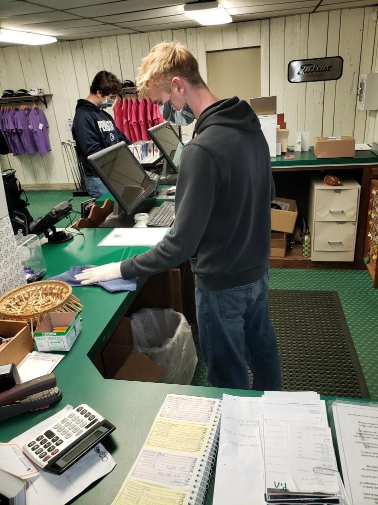 A man wearing a mask is standing at a counter in a store cleaning.