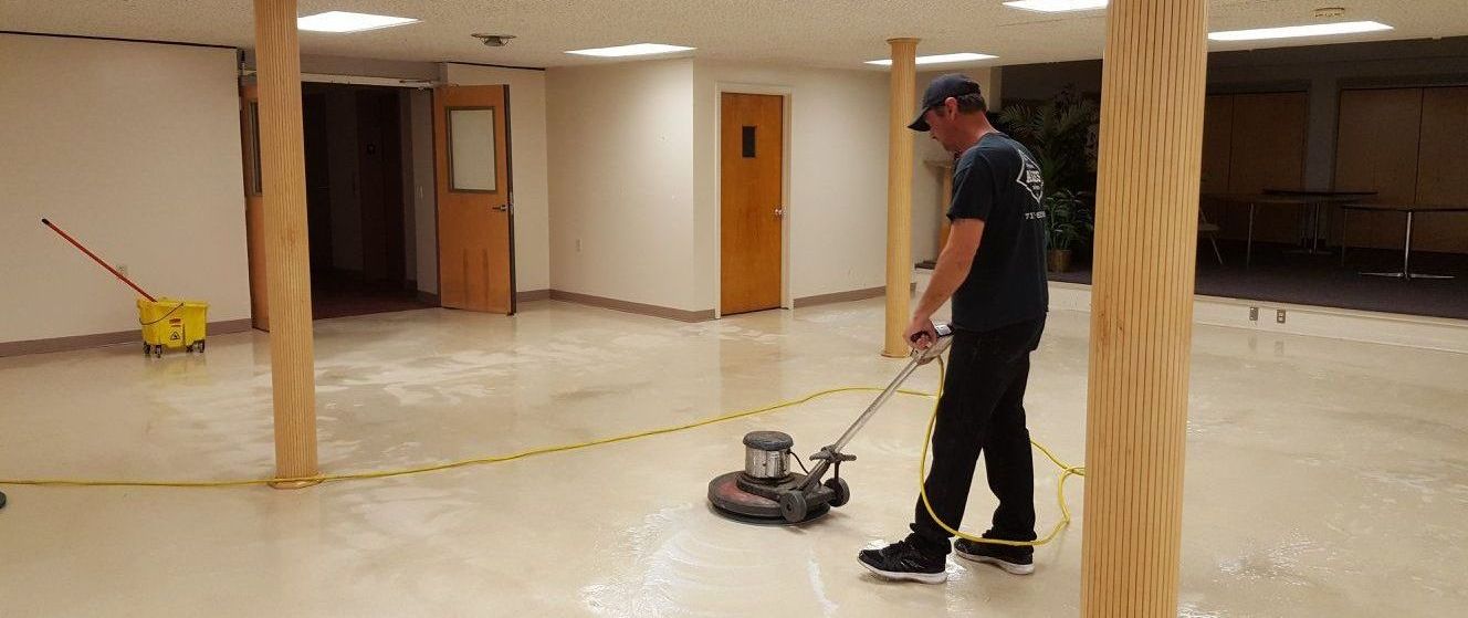 A man is cleaning the floor of an empty school room with a machine.